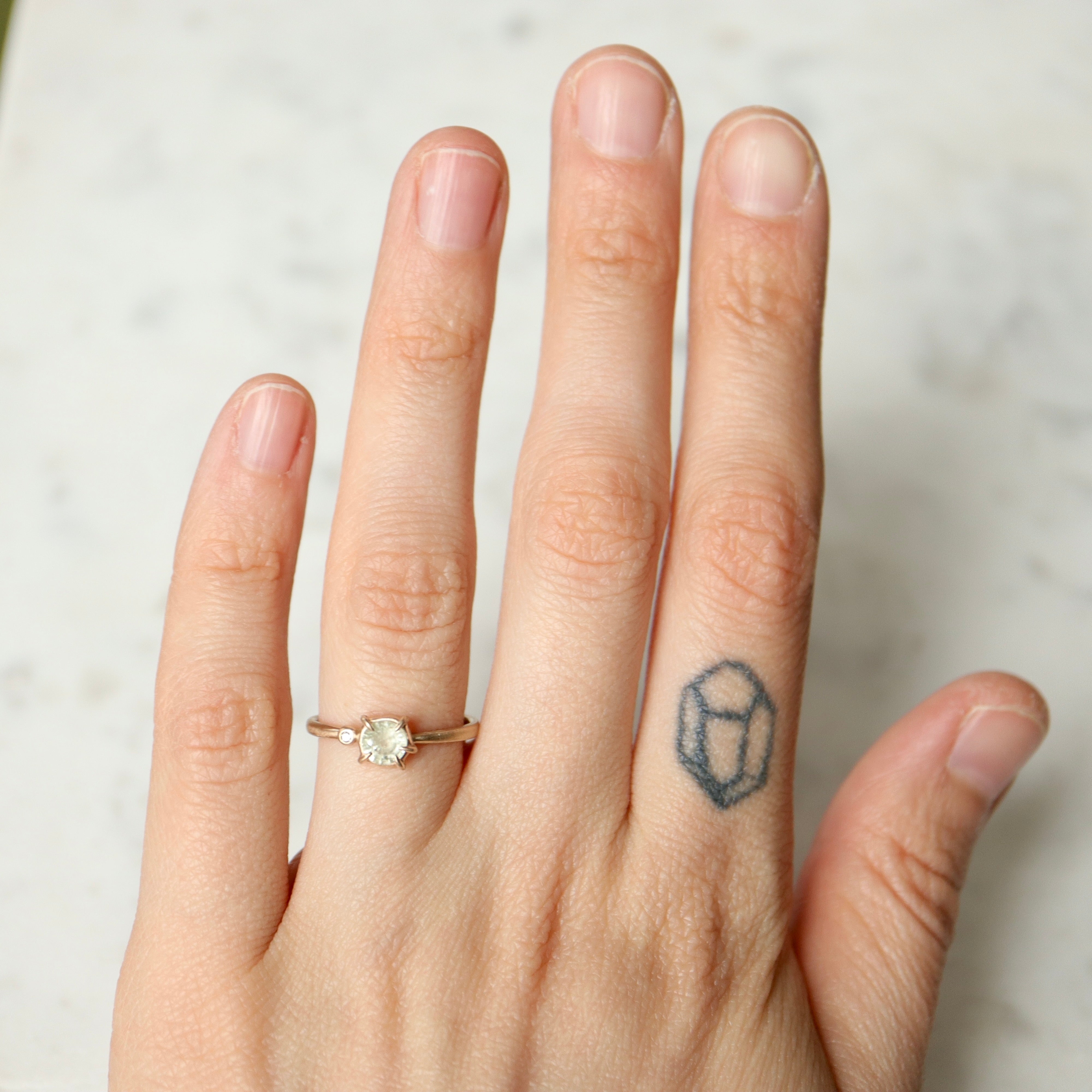 white sapphire set in a gold ring with a single white diamond on the side- on person