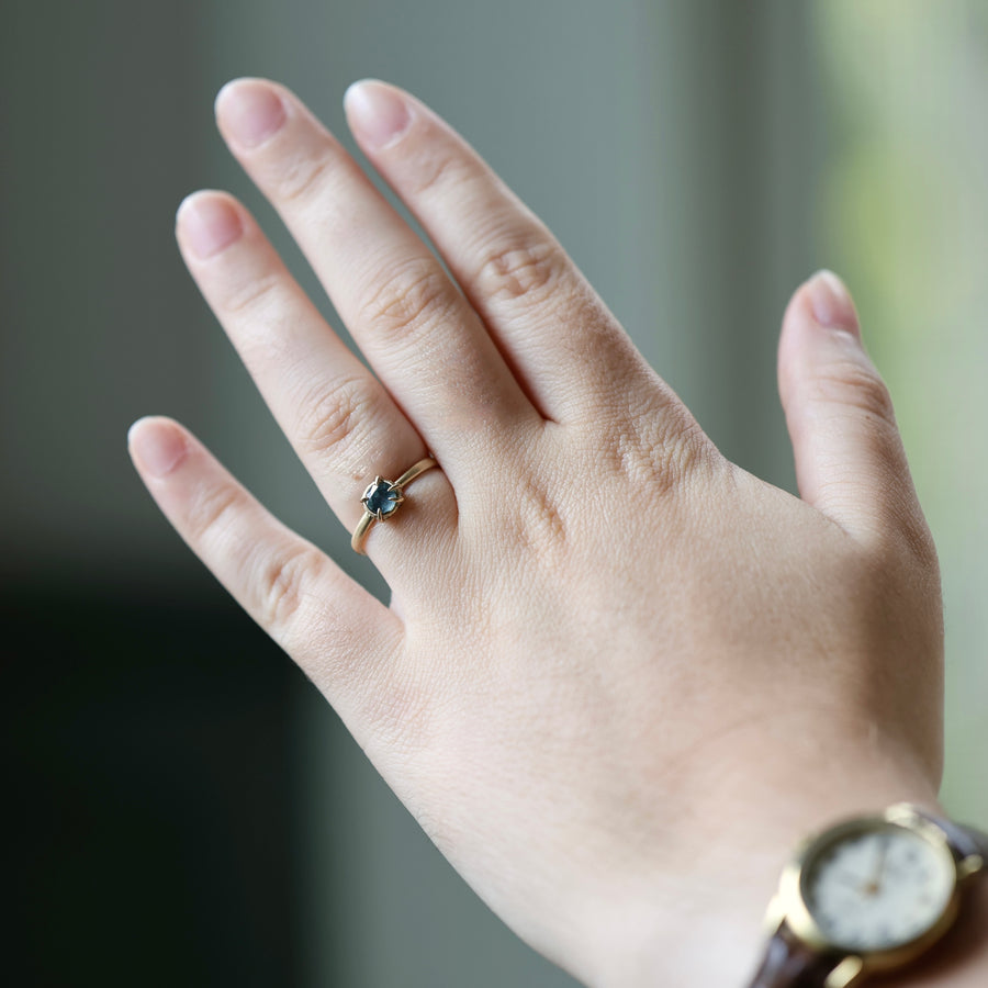 Hand wearing a ring with a blue gemstone and a gold watch on a blurred background