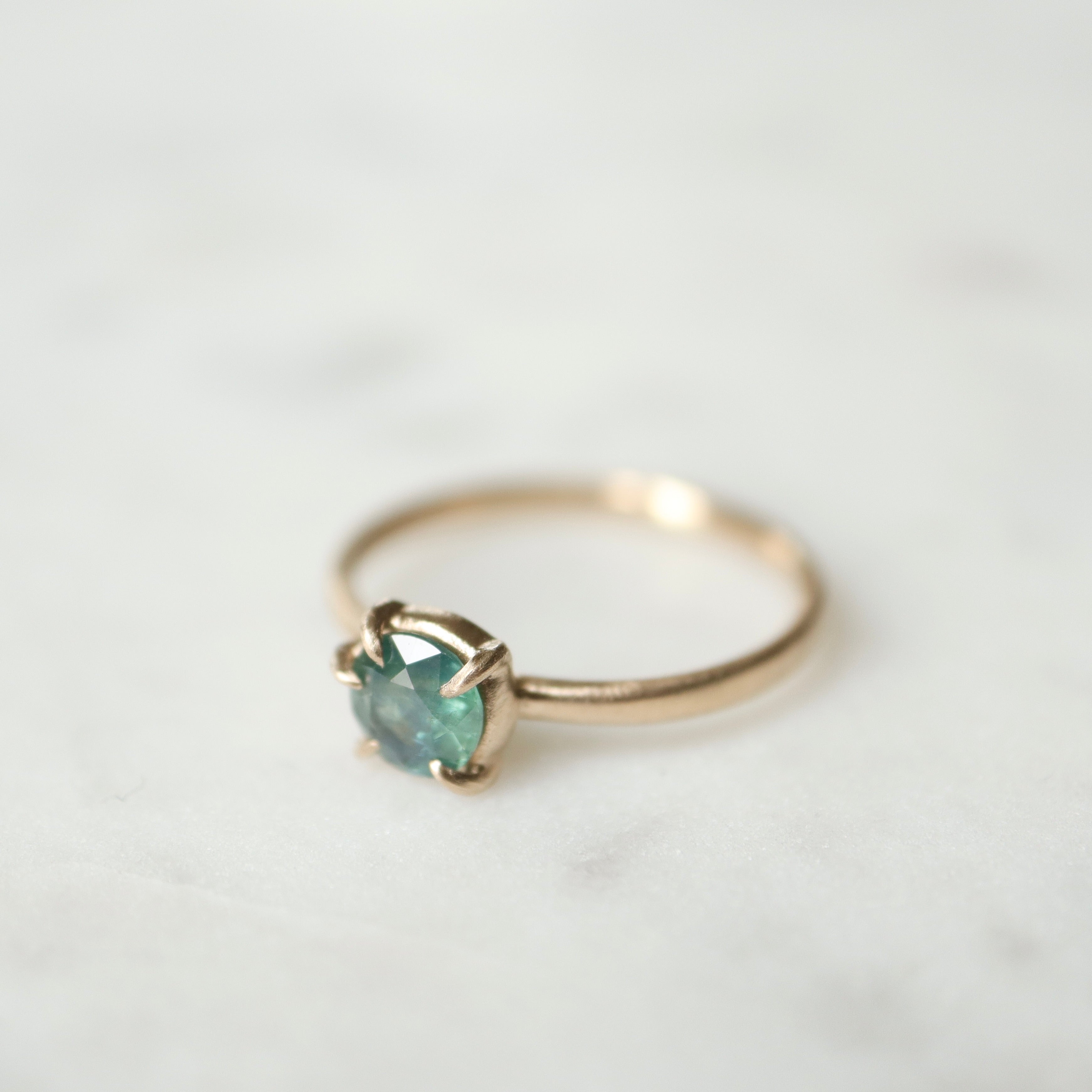 side view of teal montana sapphire set in gold prongs on a gold ring