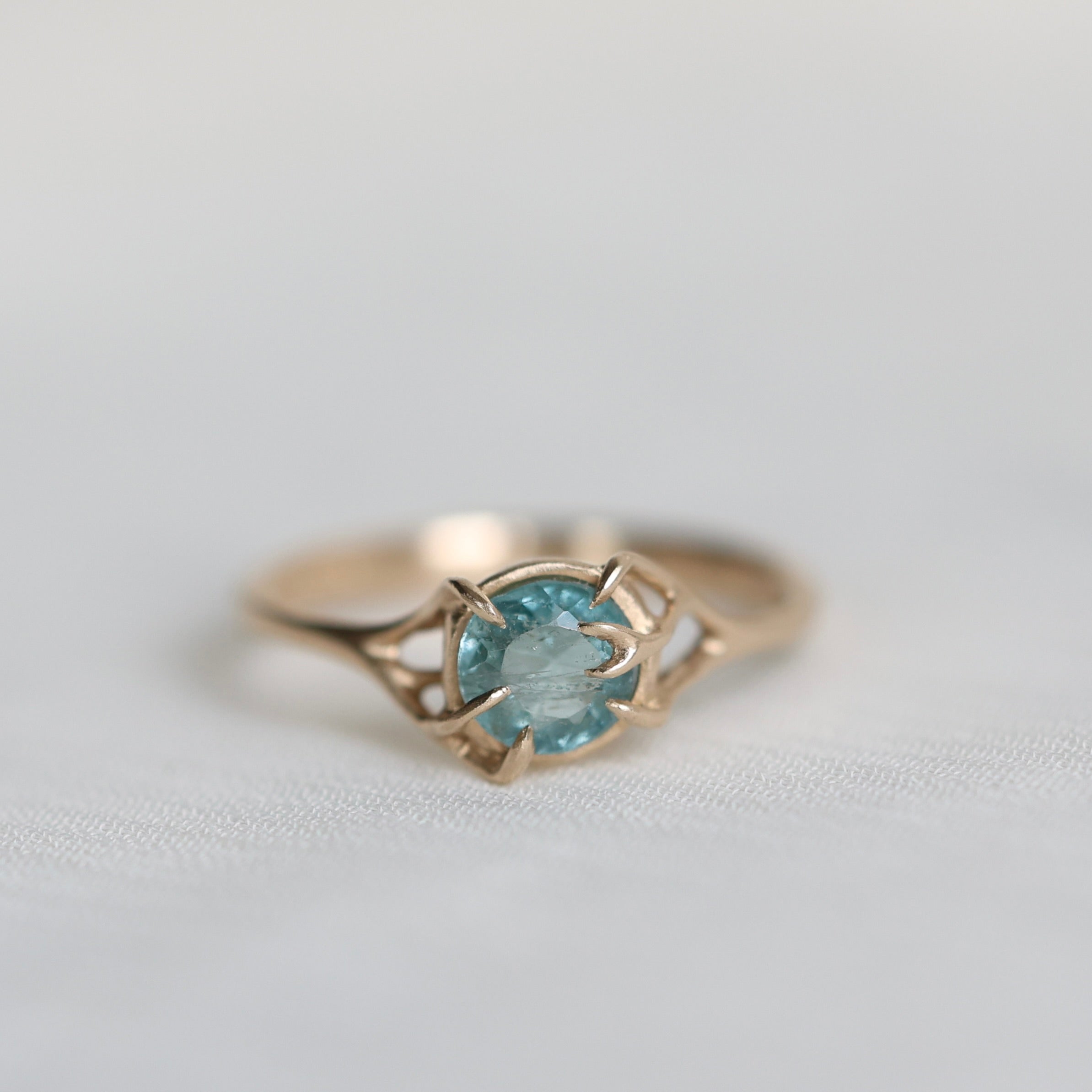 Gold ring with a blue gemstone on a light gray background