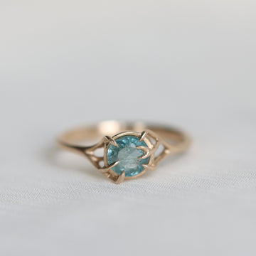 Gold ring with a blue gemstone on a light gray background