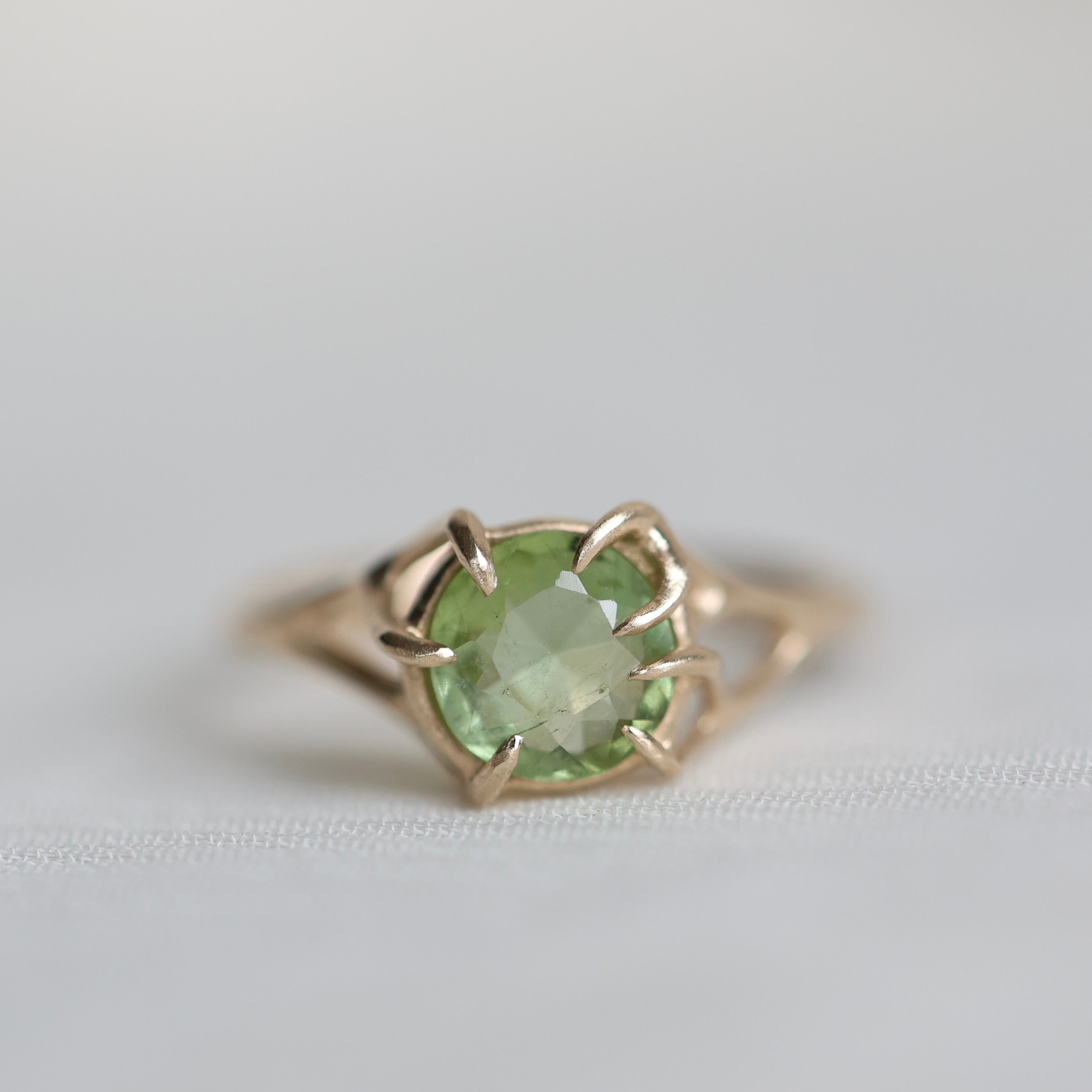Gold ring with a green gemstone on a light gray background