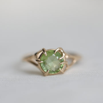 Gold ring with a green gemstone on a light gray background