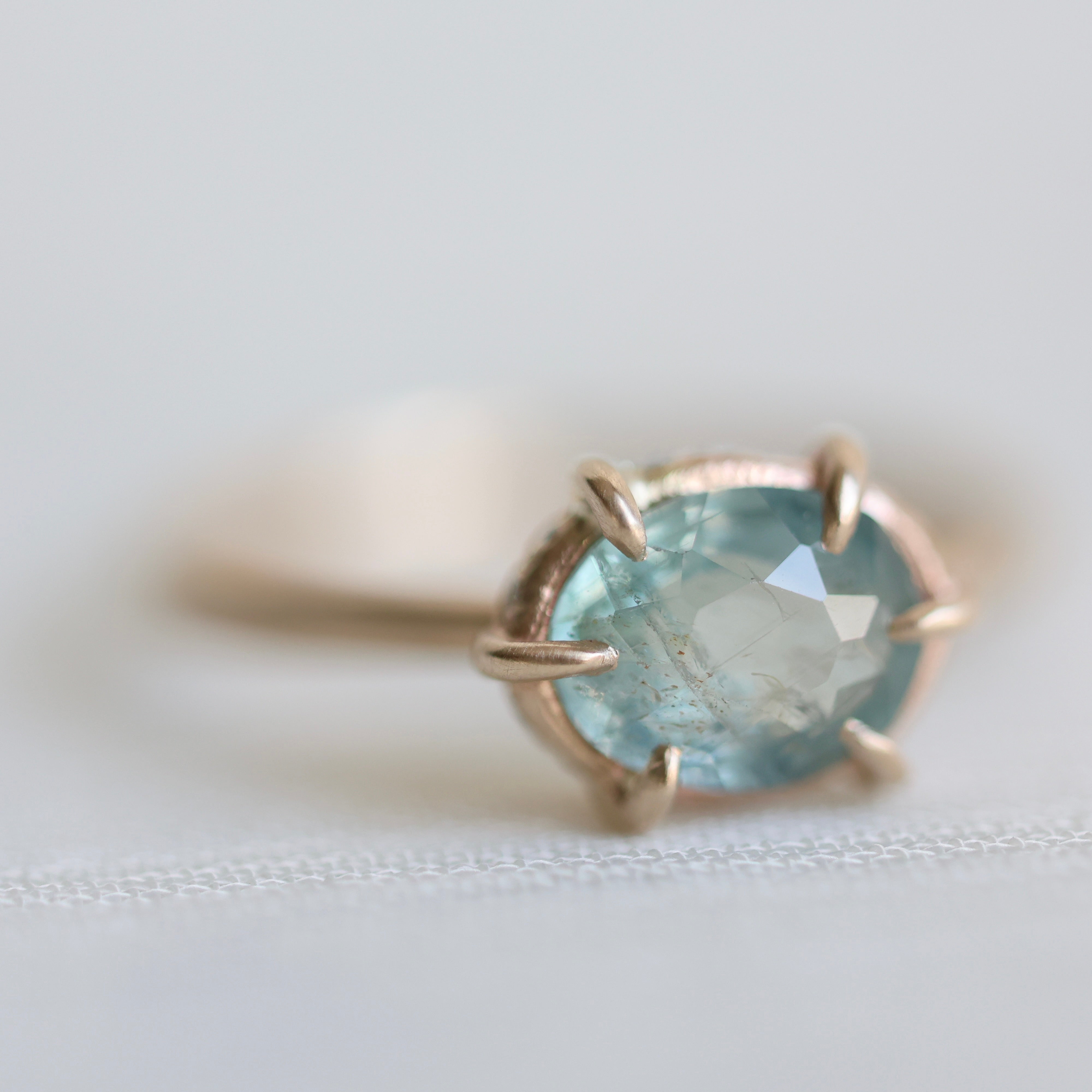 14k yellow gold ring with a light blue Montana sapphire on a soft white fabric background.