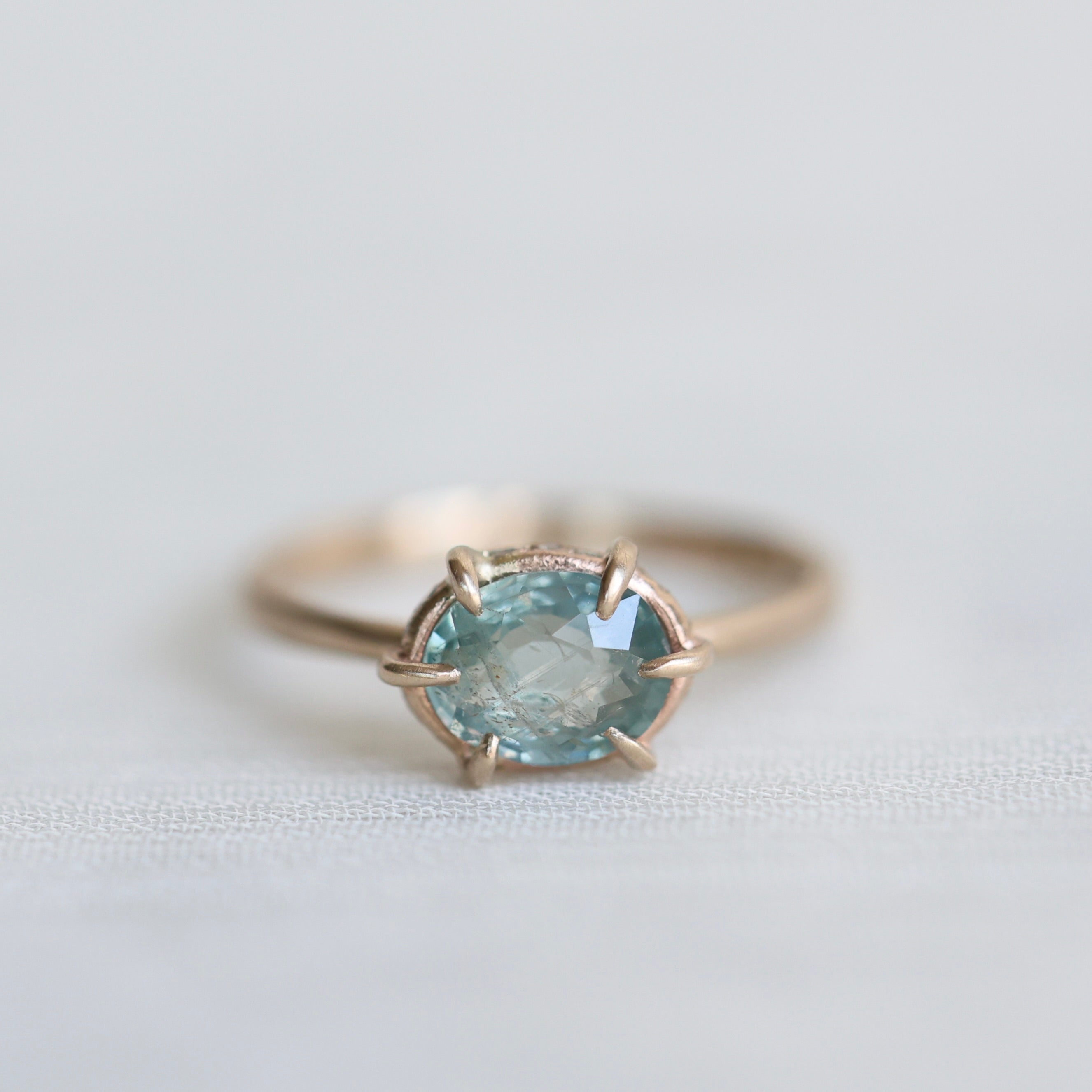 14k yellow gold ring with a light blue Montana sapphire on a soft white fabric background.