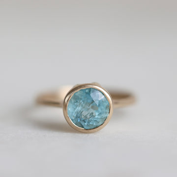 Gold ring with a blue gemstone on a light gray background