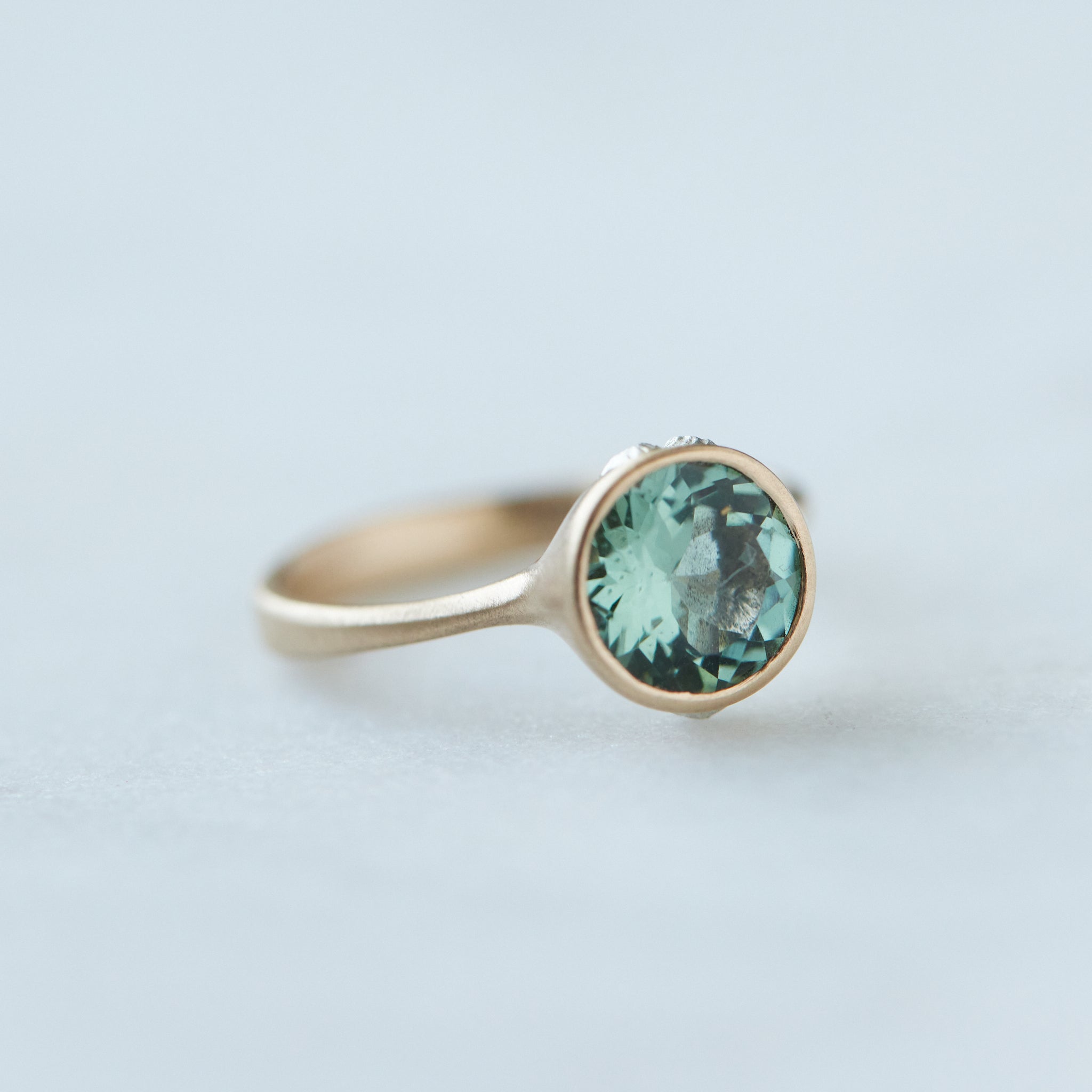 A round, icy mint tourmaline is set in a gold bezel ring with silver barnacles. Side view.