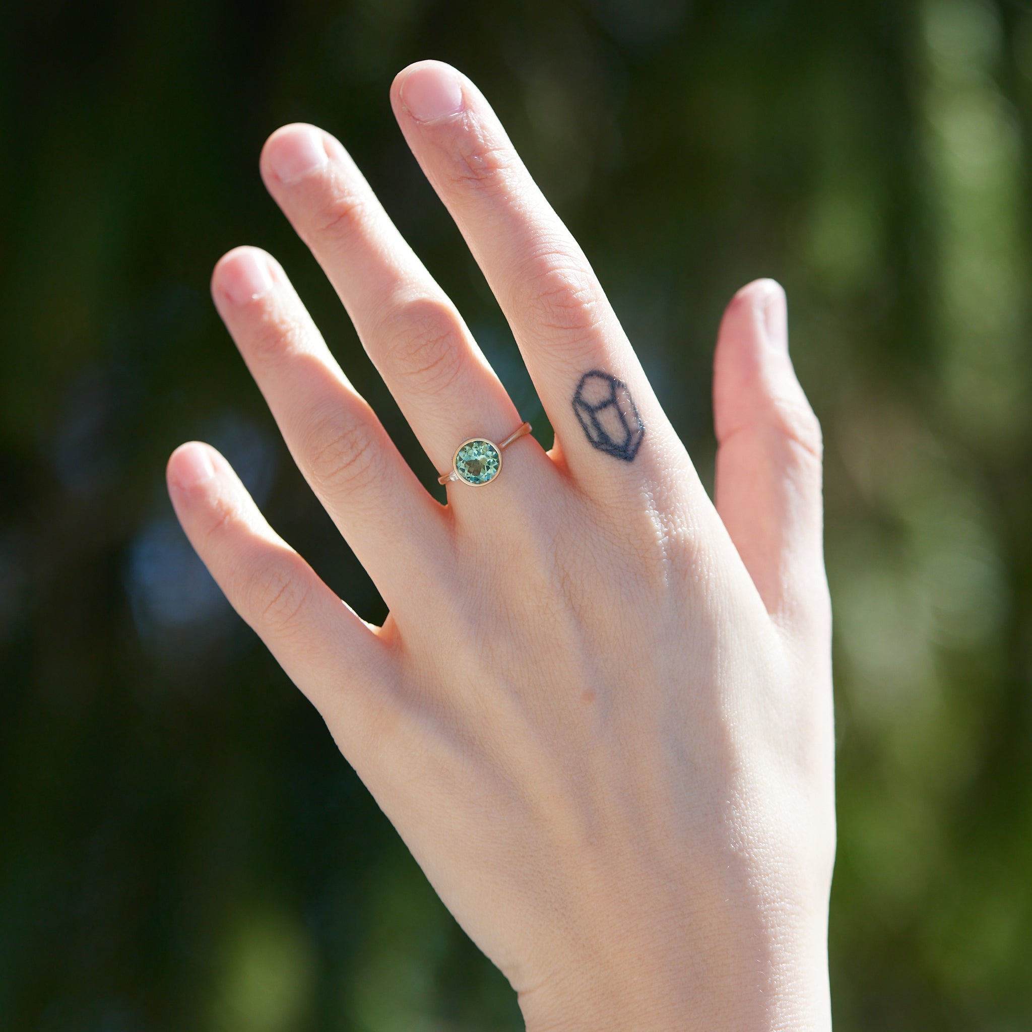 A round, icy mint tourmaline is set in a gold bezel ring with silver barnacles. Photographed on person.