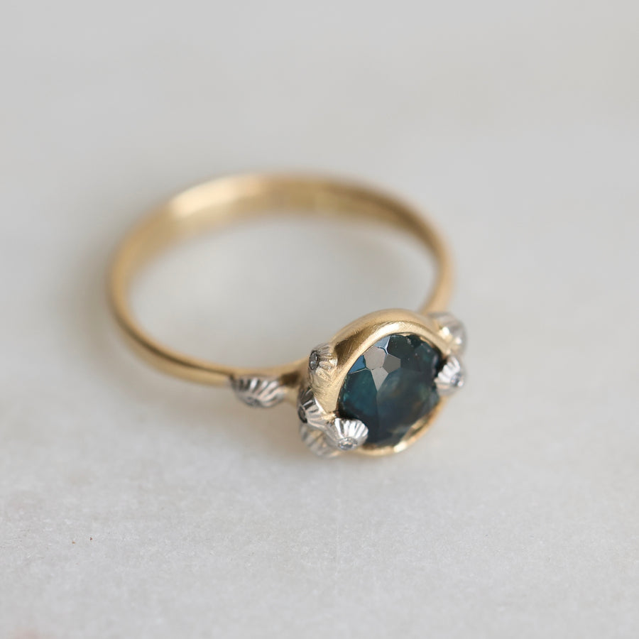 Gold ring with a teal gemstone and diamond barnacle accents on a light gray background