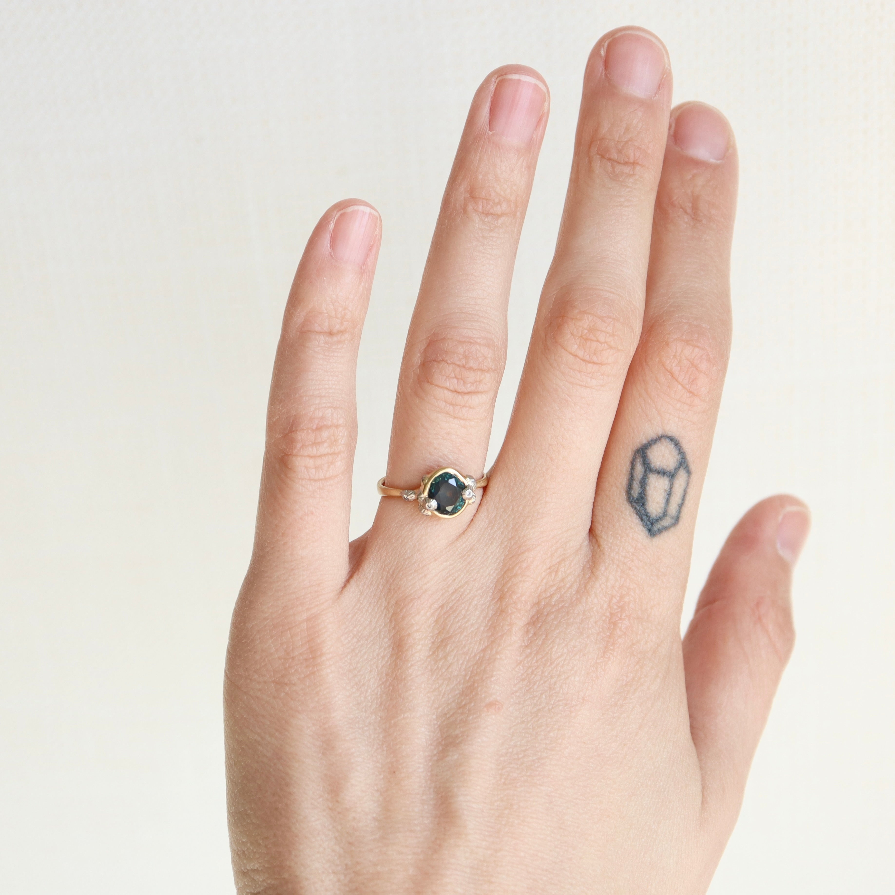 Hand wearing a ring with a gemstone on a plain background