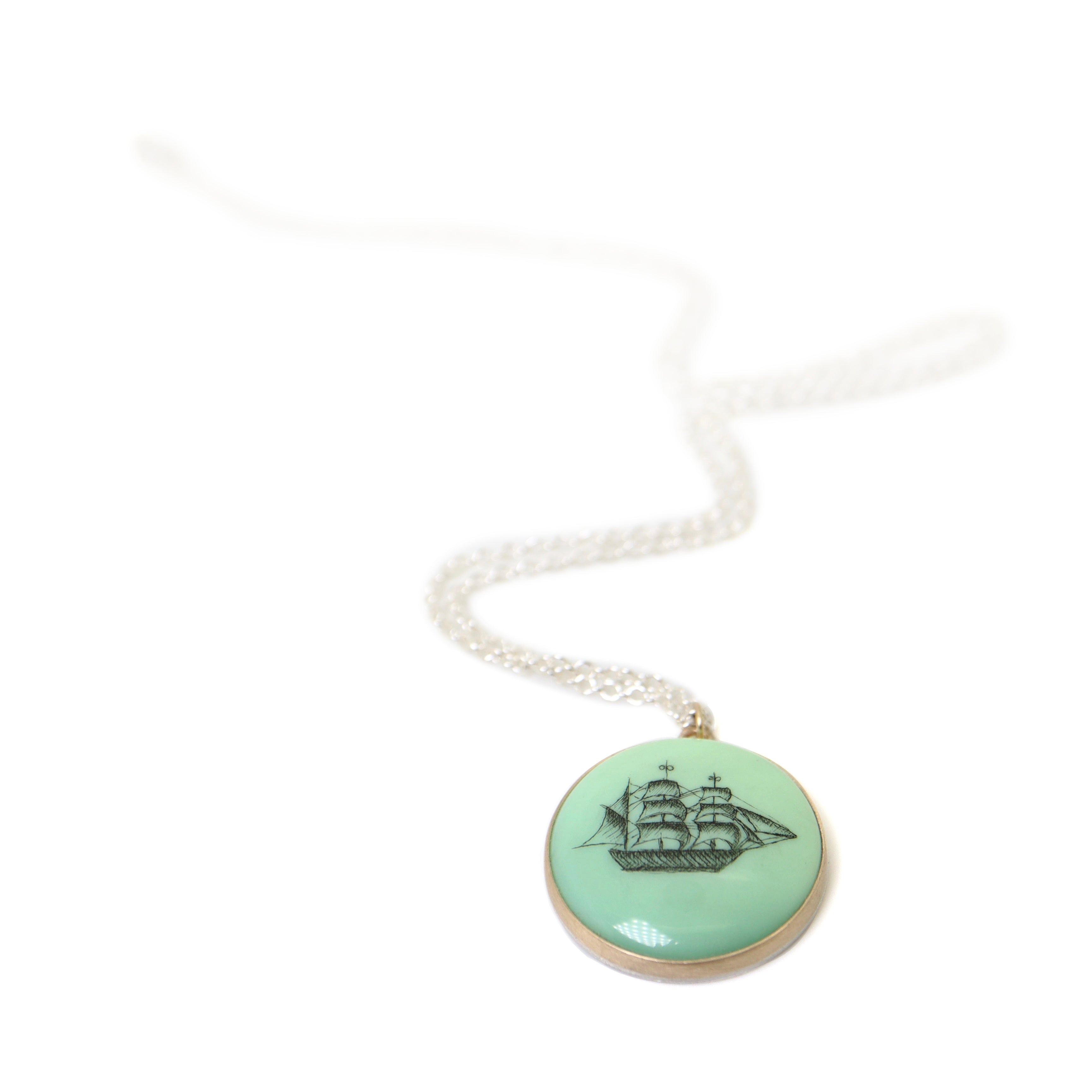 melon green round variscite cabochon is set in a gold bezel and hangs beneath a silver chain. an old whaling ship is hand-etched into the surface with black ink.