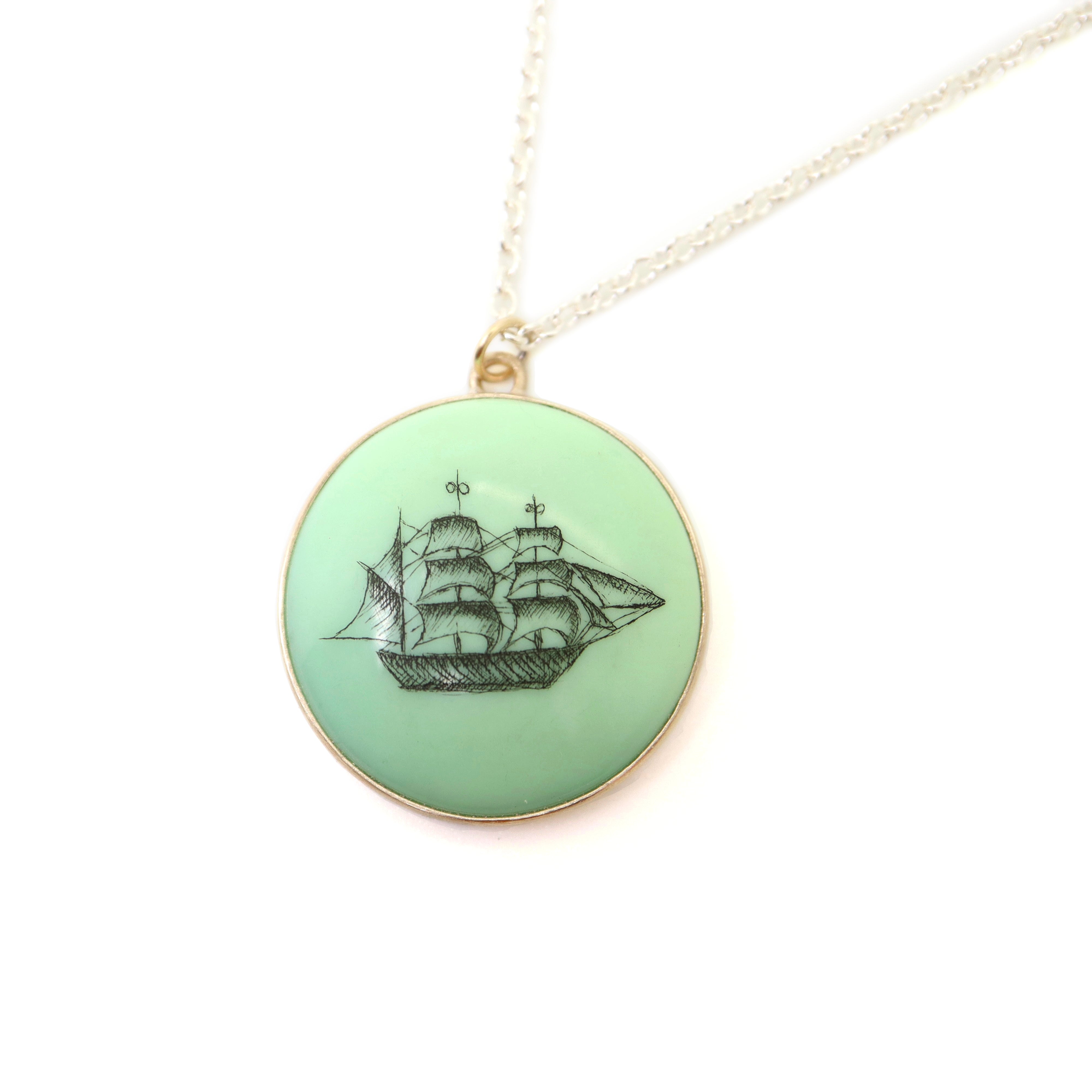 melon green round variscite cabochon is set in a gold bezel and hangs beneath a silver chain. an old whaling ship is hand-etched into the surface with black ink.