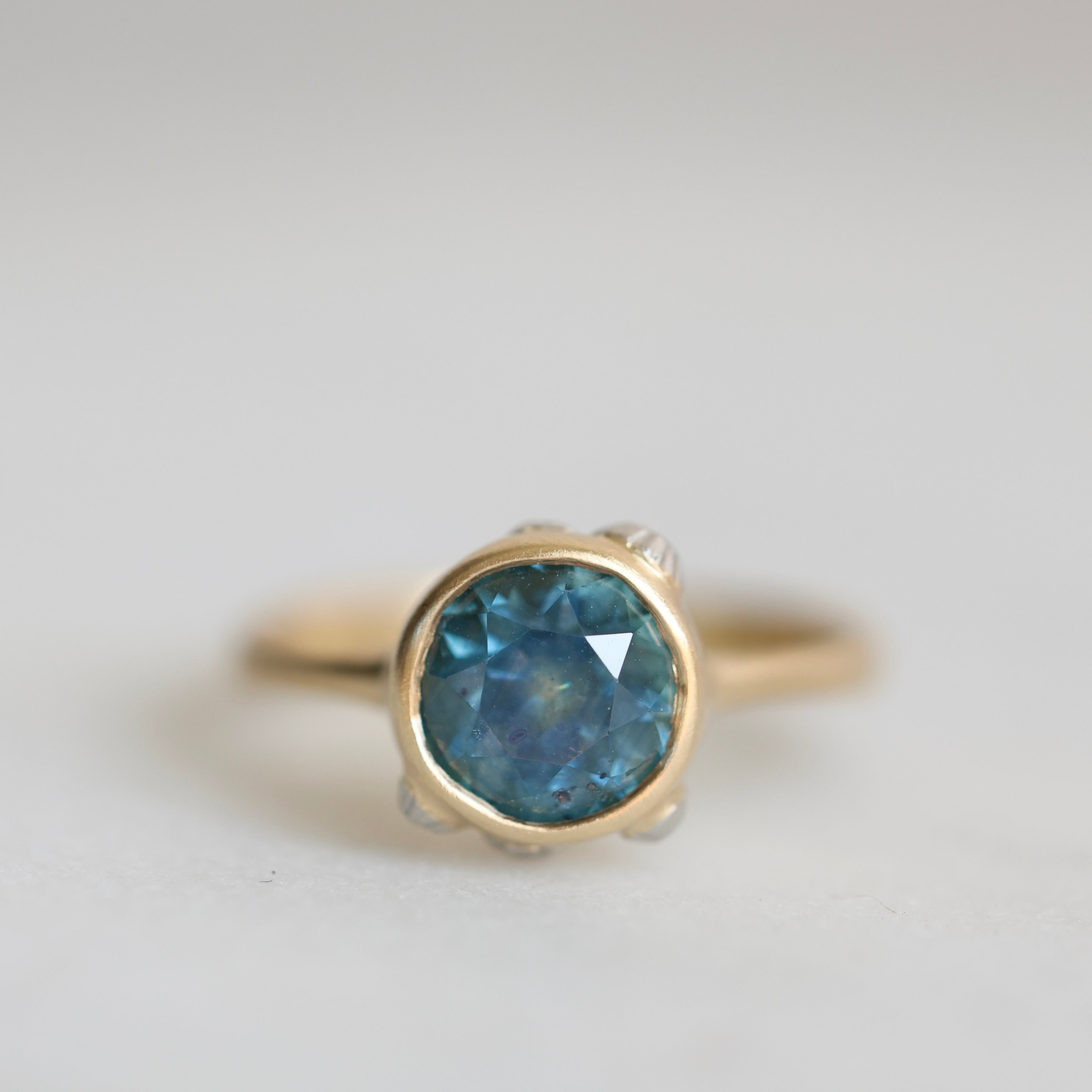 Gold ring with a blue gemstone on a light gray background