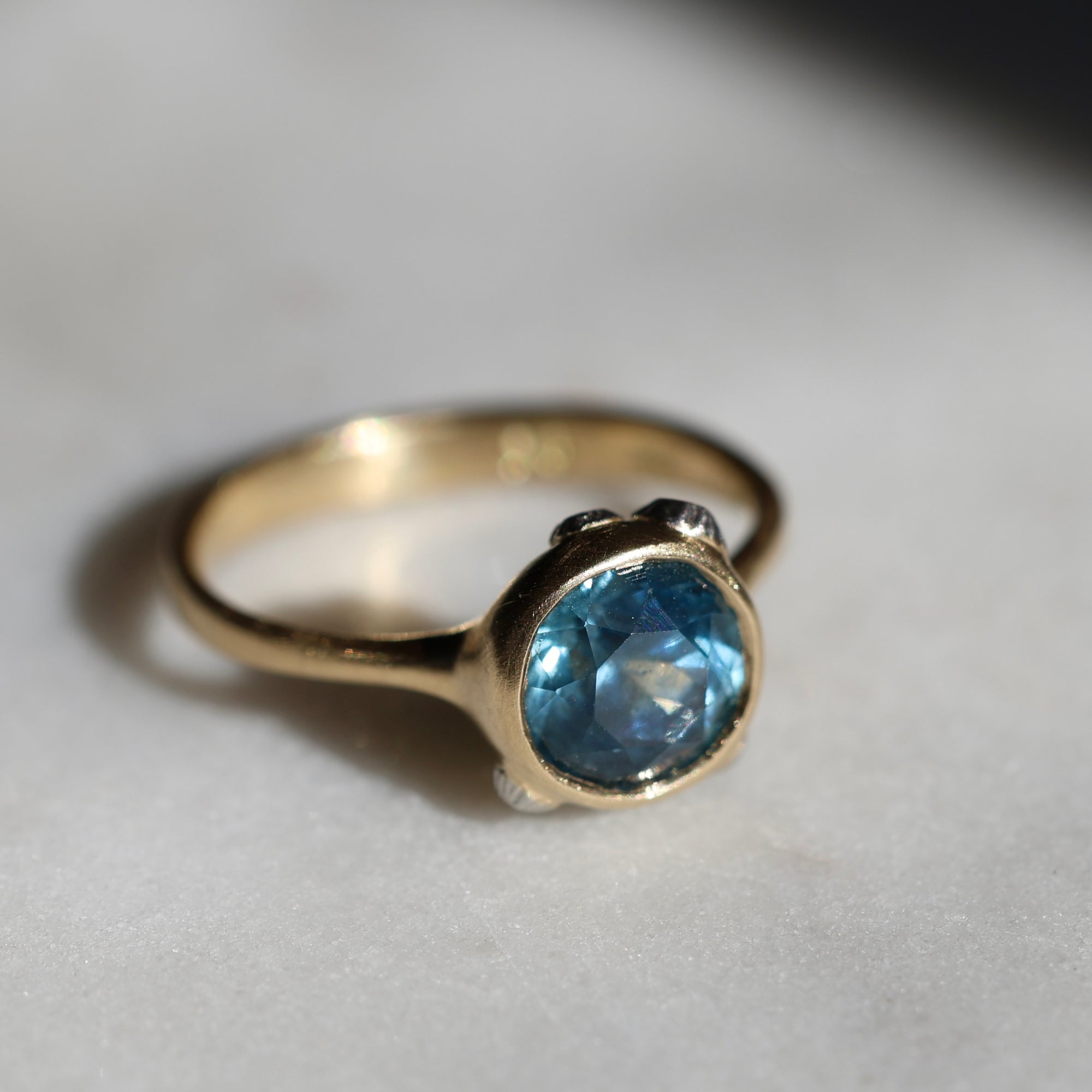 Gold ring with a blue gemstone on a light gray background