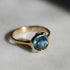 Gold ring with a blue gemstone on a light gray background