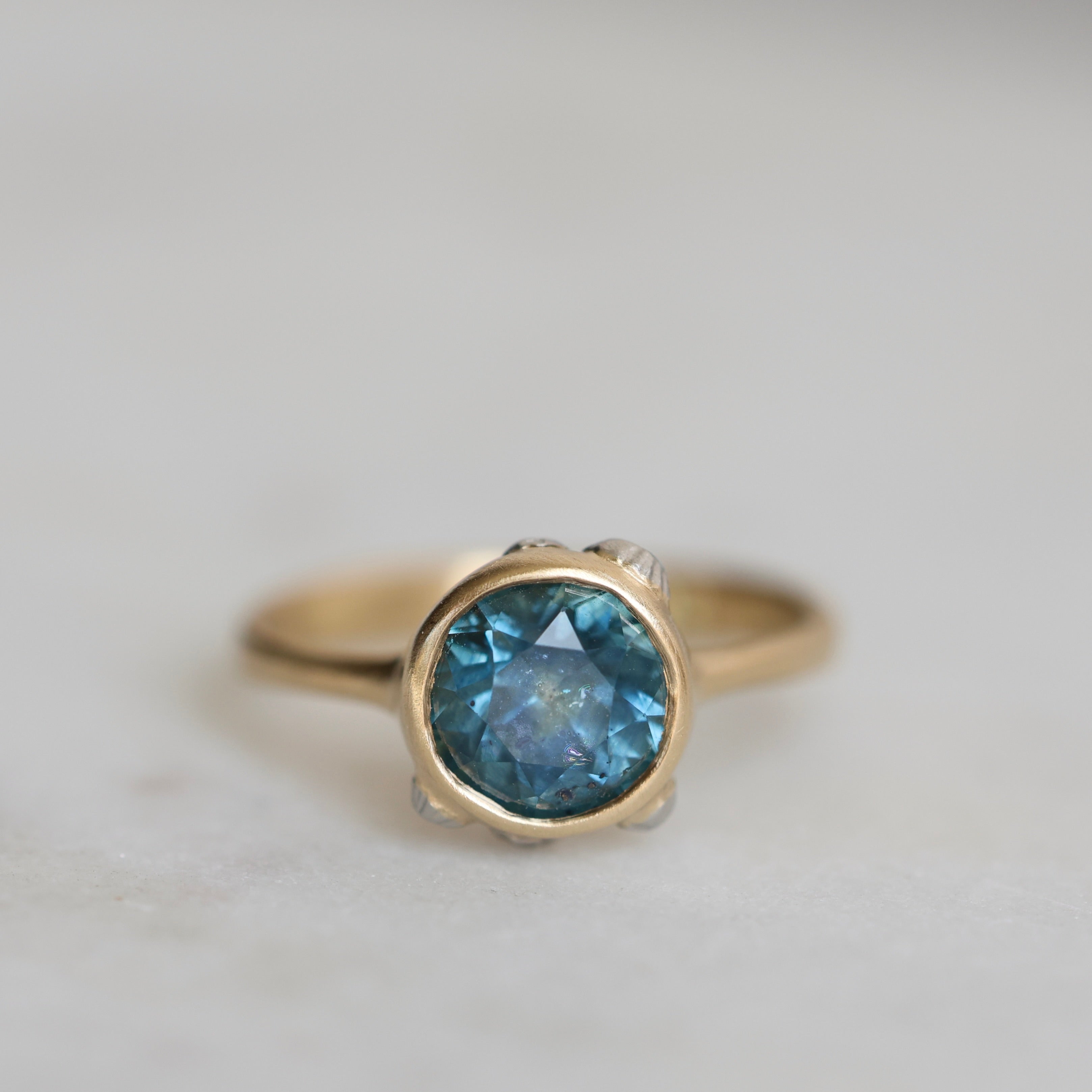 Gold ring with a blue gemstone on a light gray background