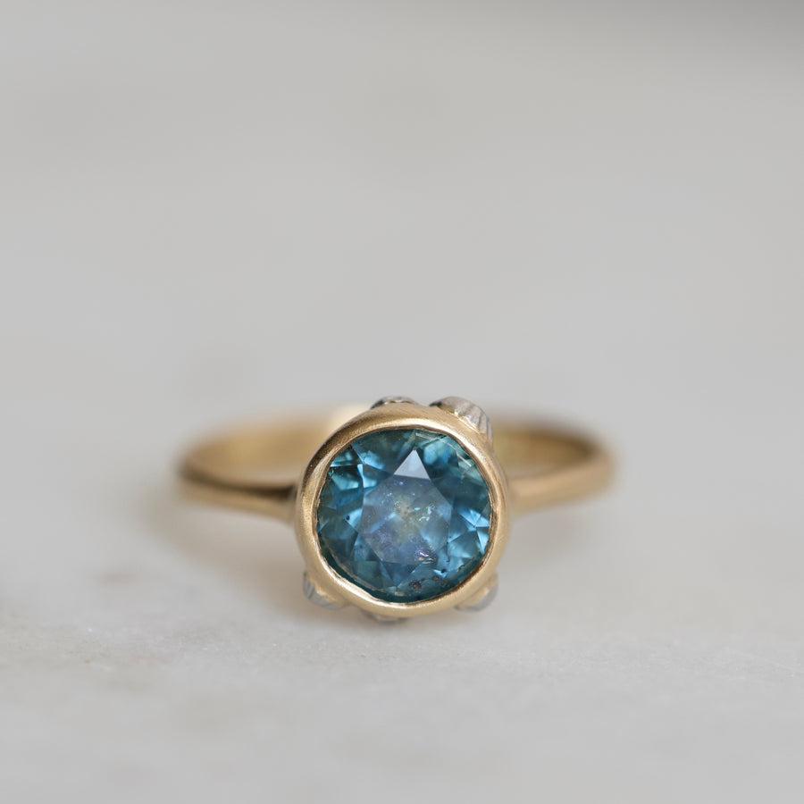 Gold ring with a blue gemstone on a light gray background