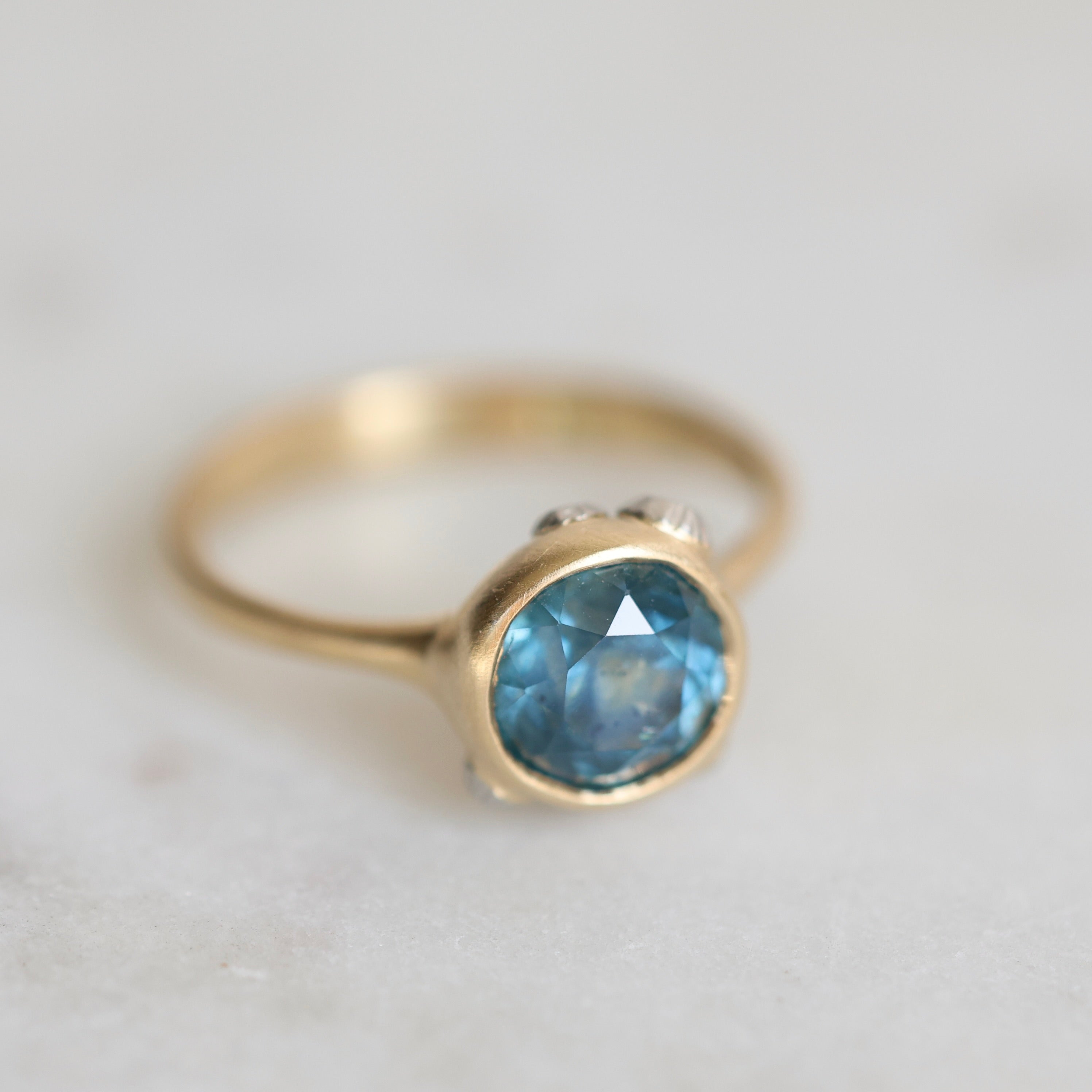 Gold ring with a blue gemstone on a light gray background