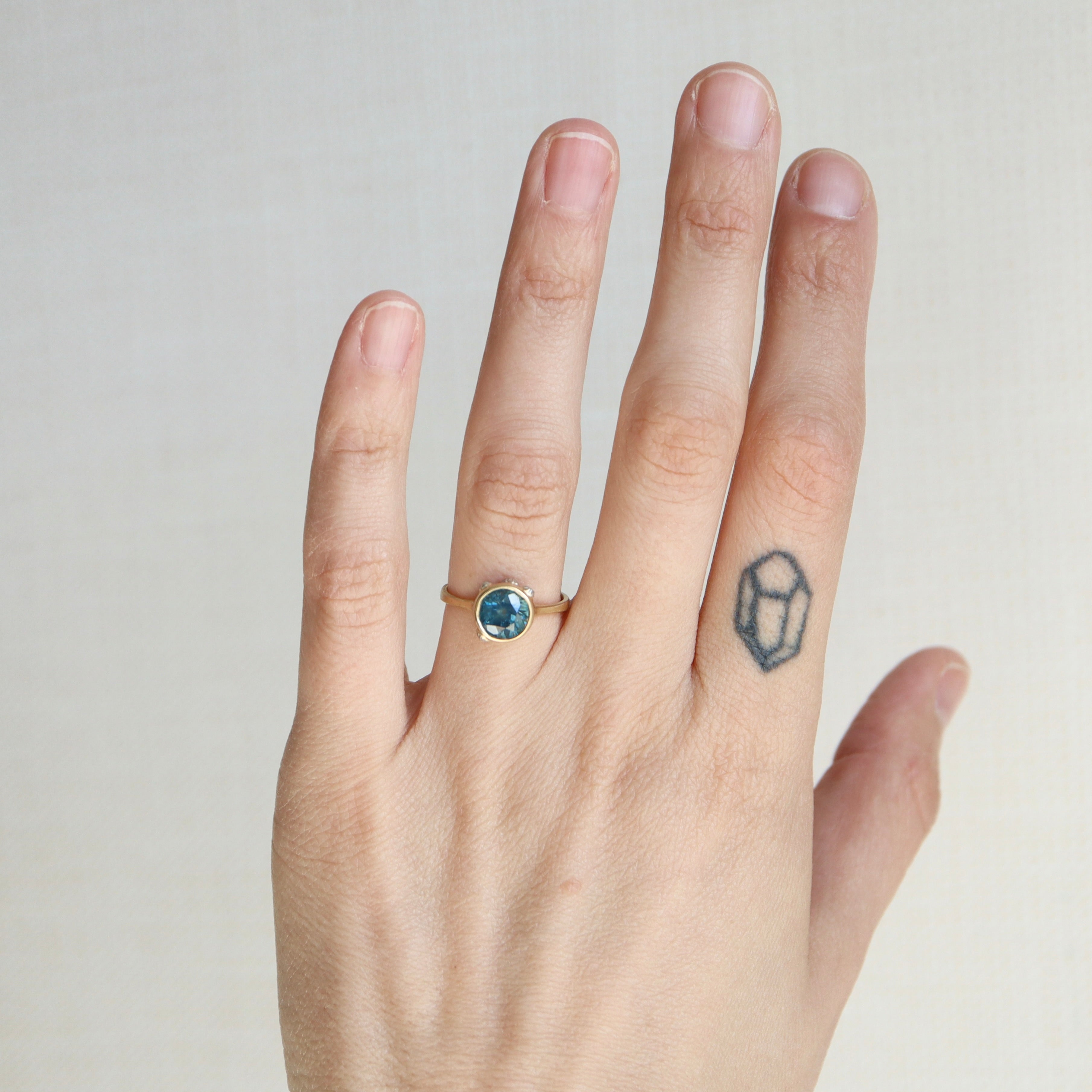 Hand wearing a ring with a blue gemstone on a plain background