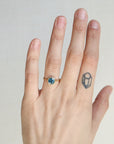 Hand wearing a ring with a blue gemstone on a plain background