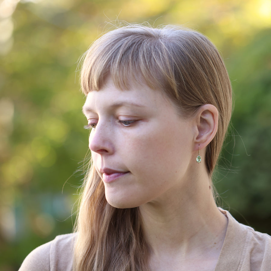 Woman with blond hair and bangs, wearing earrings against a blurred green background