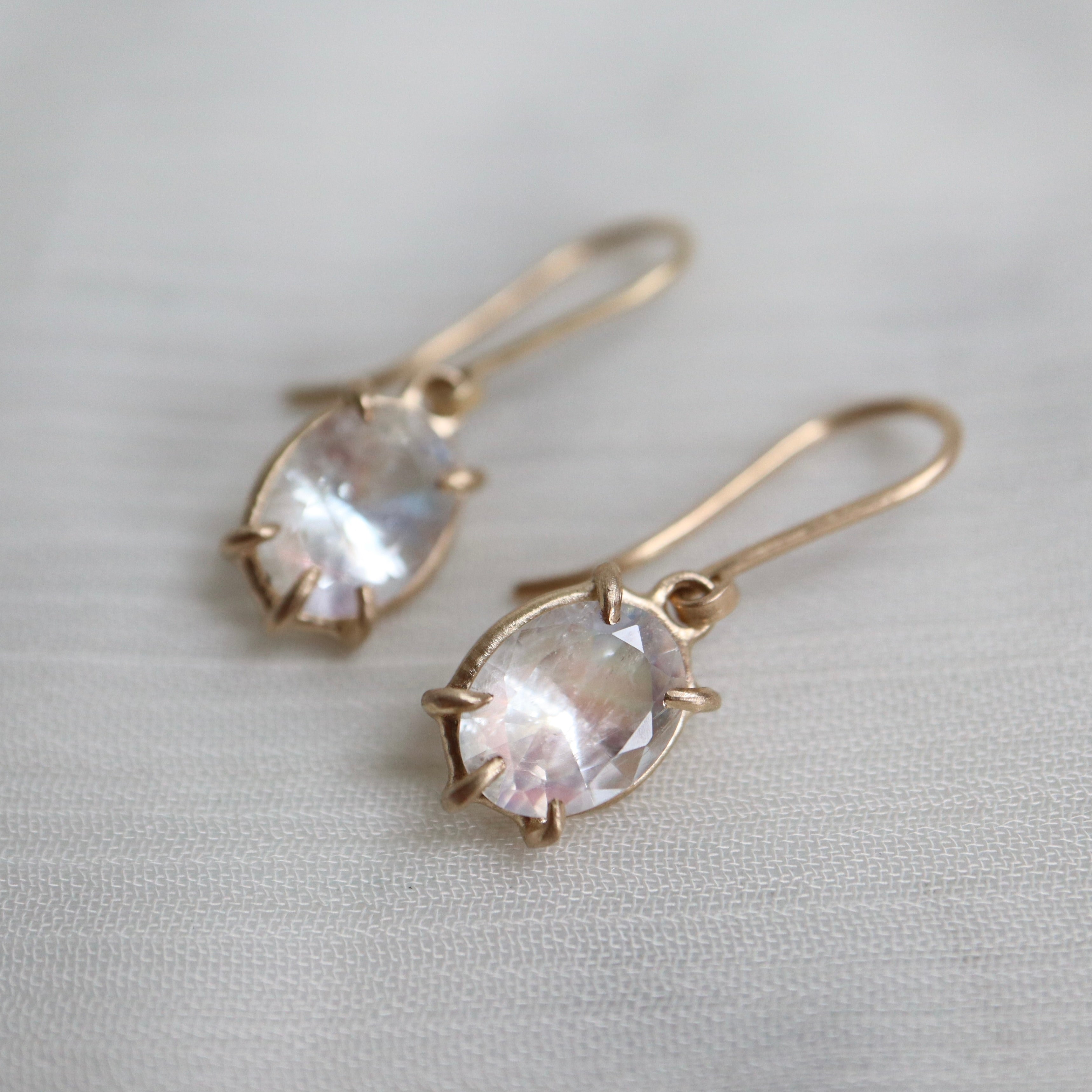 a pair of earrings features oval rainbow moonstones set in gold prongs