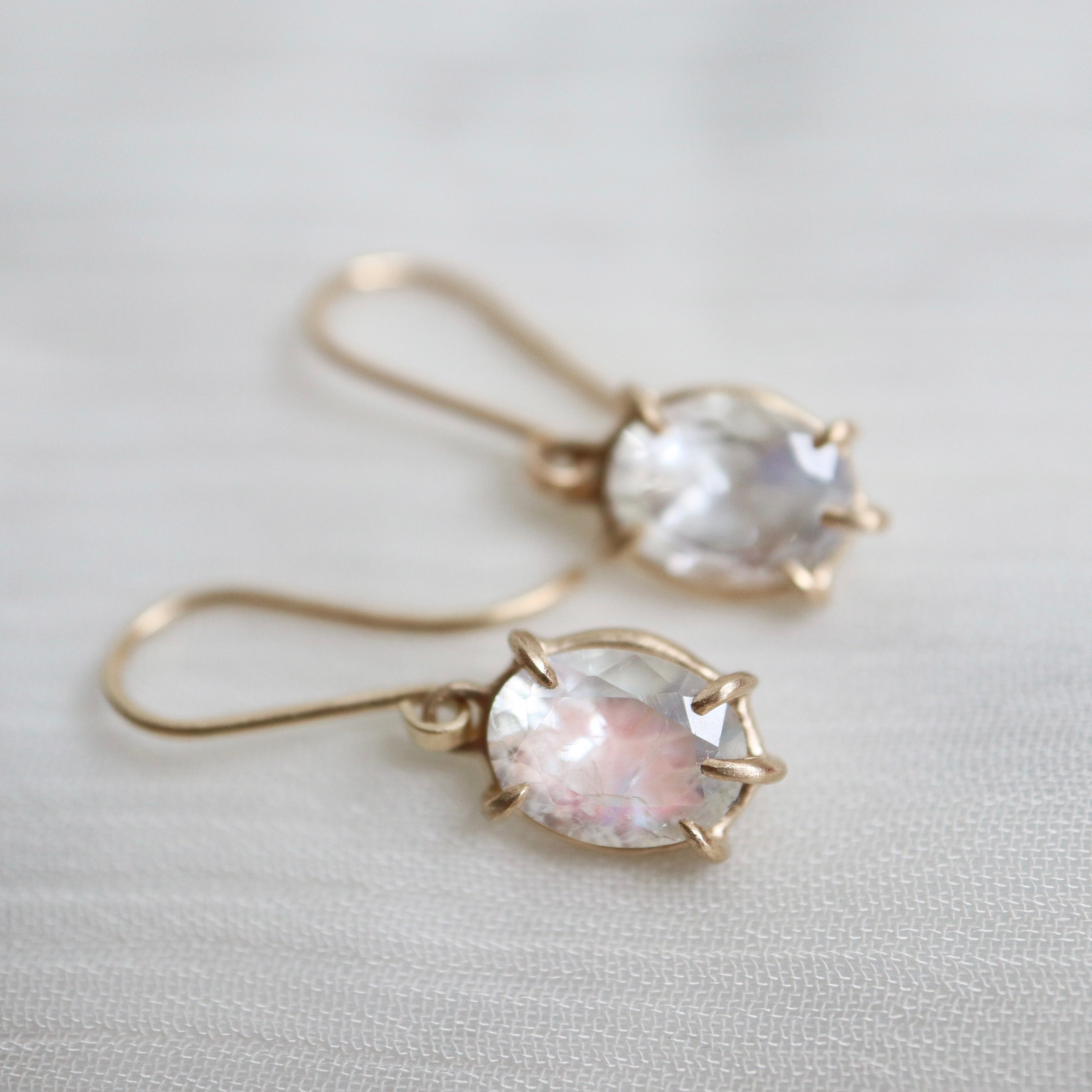 a pair of earrings features oval rainbow moonstones set in gold prongs