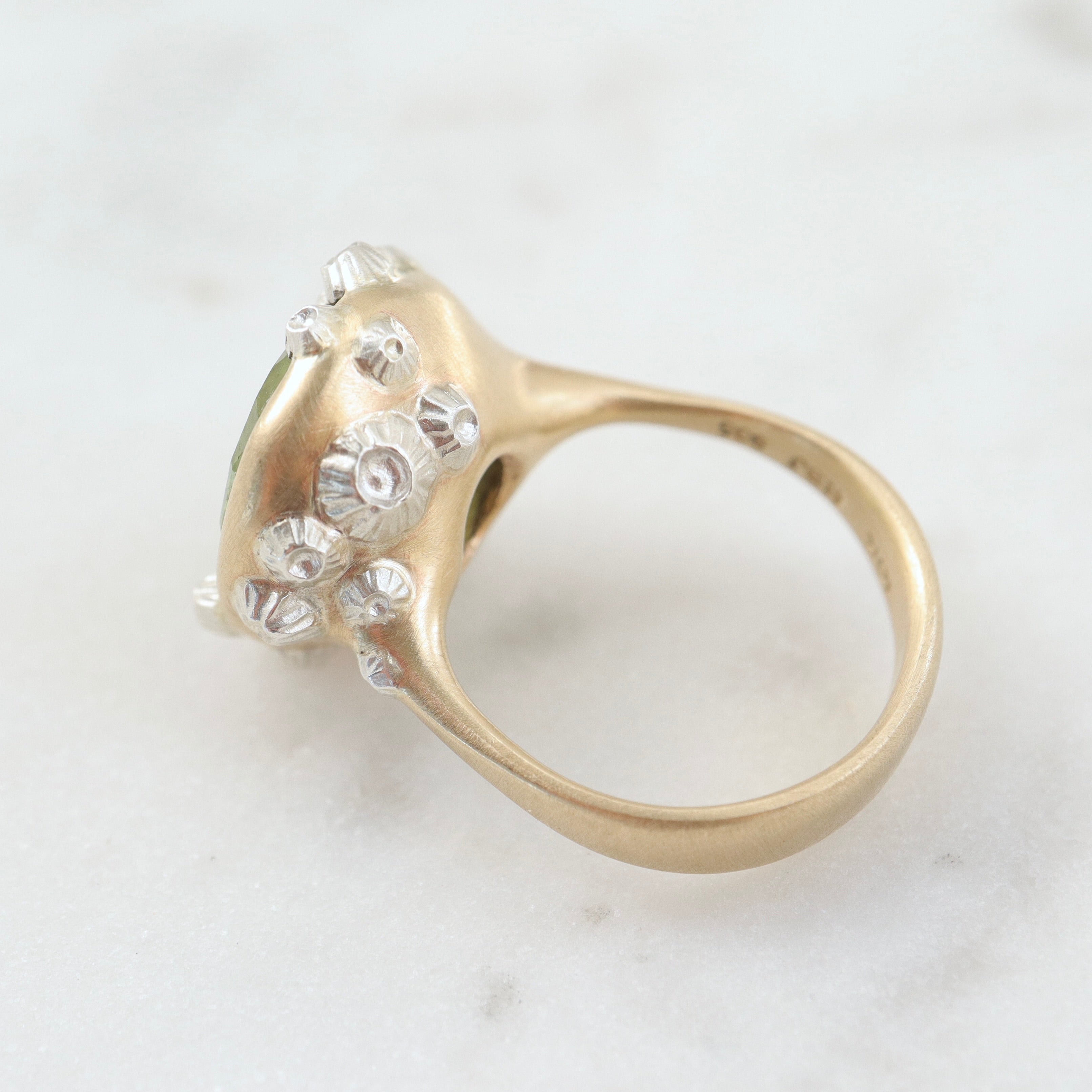 a lime green, rough-hewn tourmaline gemstone is set in a light yellow gold. Lots of little silver barnacles wrap around the setting and up over the stone. back view.