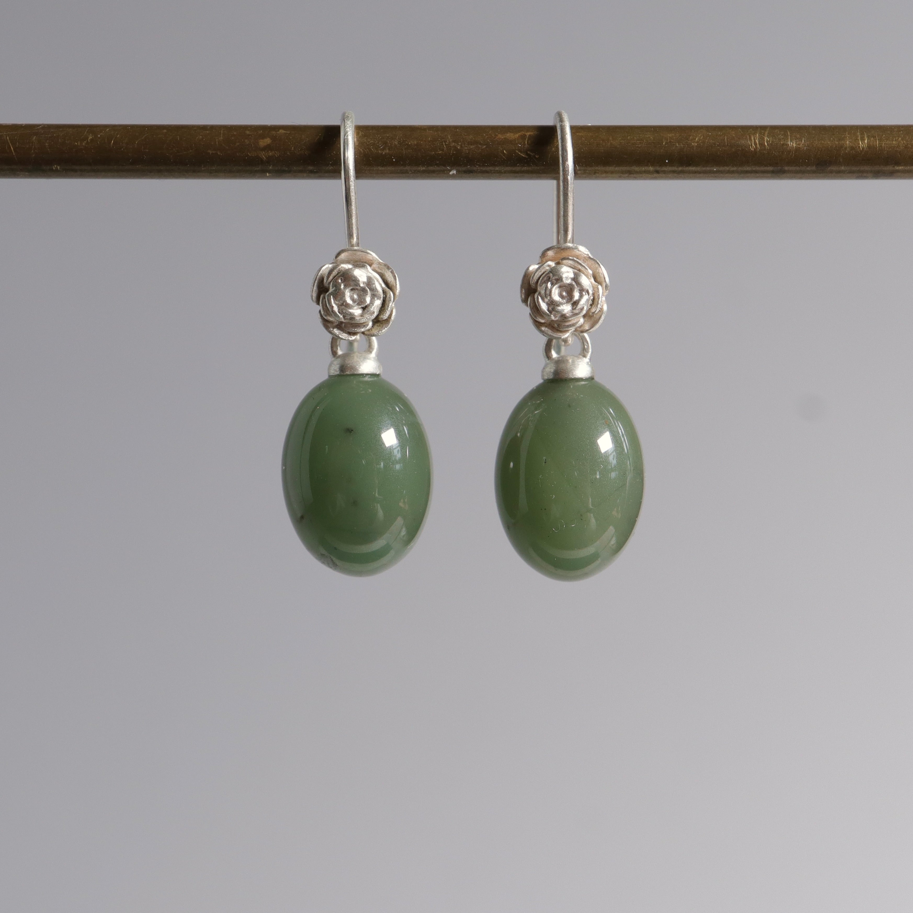 sage green jade oval beads hang beneath silver ear wires featuring little silver roses on them