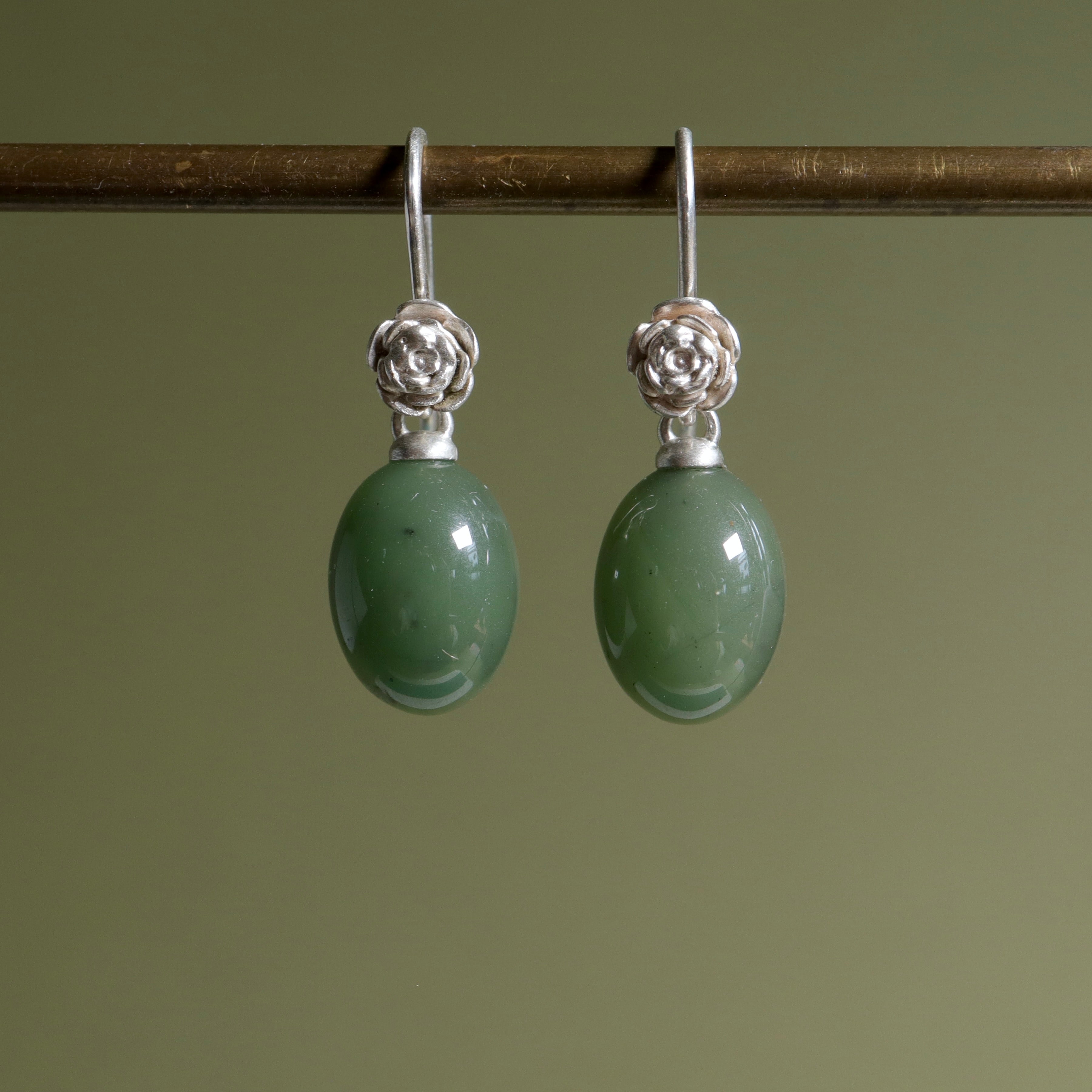 sage green jade oval beads hang beneath silver ear wires featuring little silver roses on them