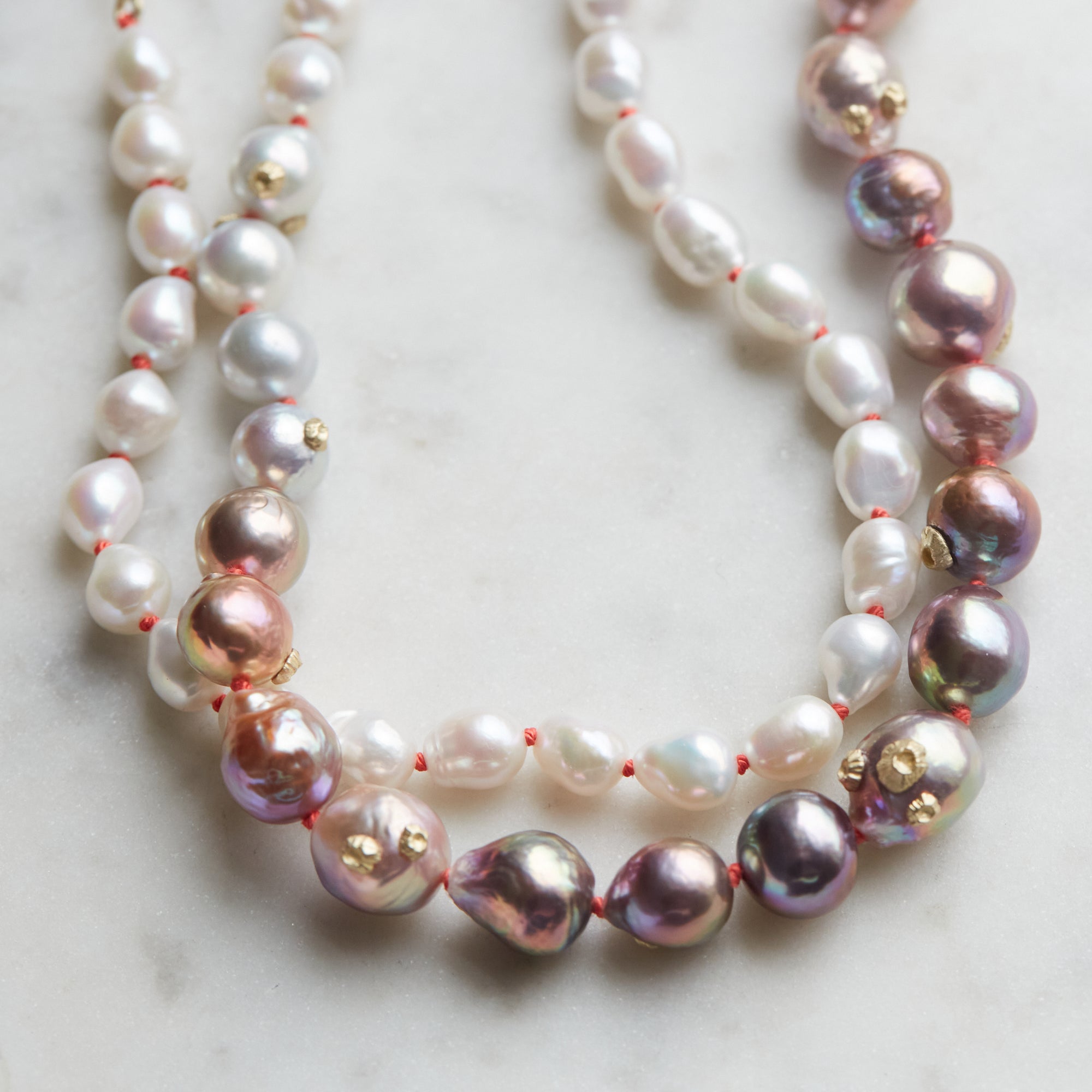 detail of pink and white freshwater baroque pearl necklace in ombre pattern with gold barnacles and fish hook clasp and coral silk by hannah blount jewelry