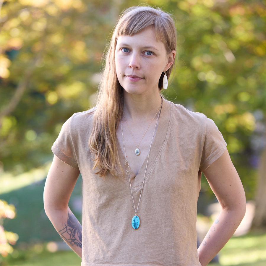 Woman wearing a beige shirt with two necklaces outdoors