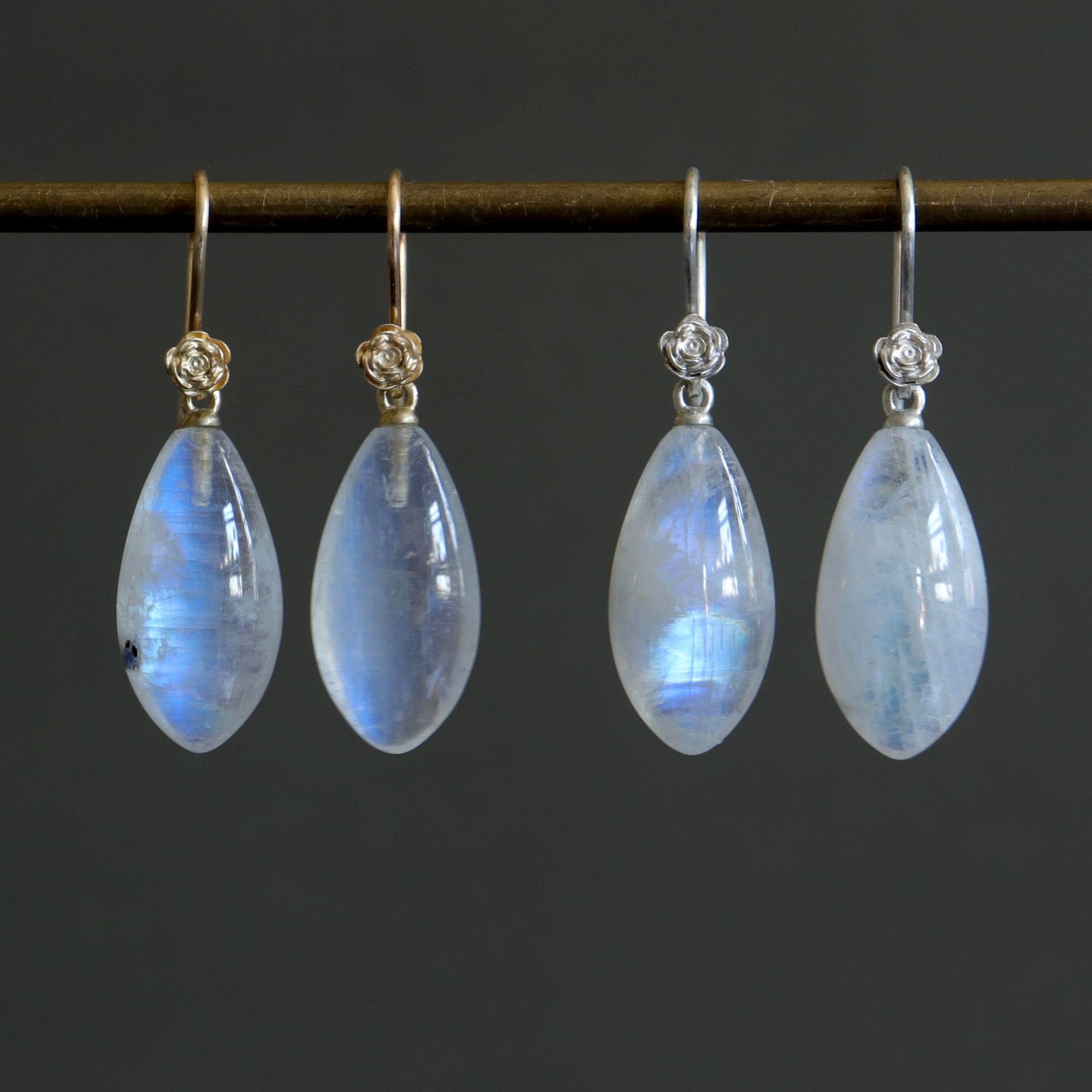 two pairs of moonstone drop earrings. One pair has silver ear wires with roses and one pair has gold ear wires and roses.