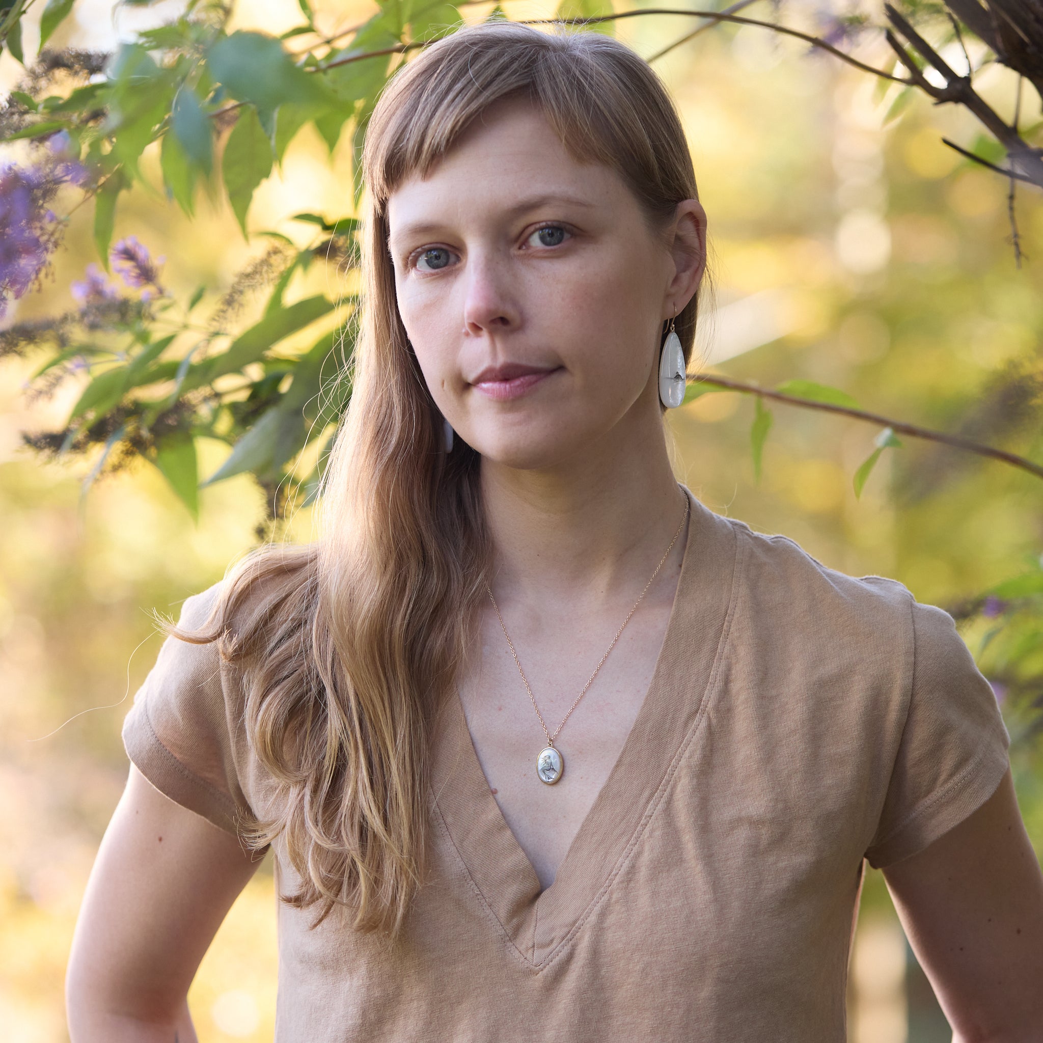 Woman standing outdoors with blurred greenery in the background