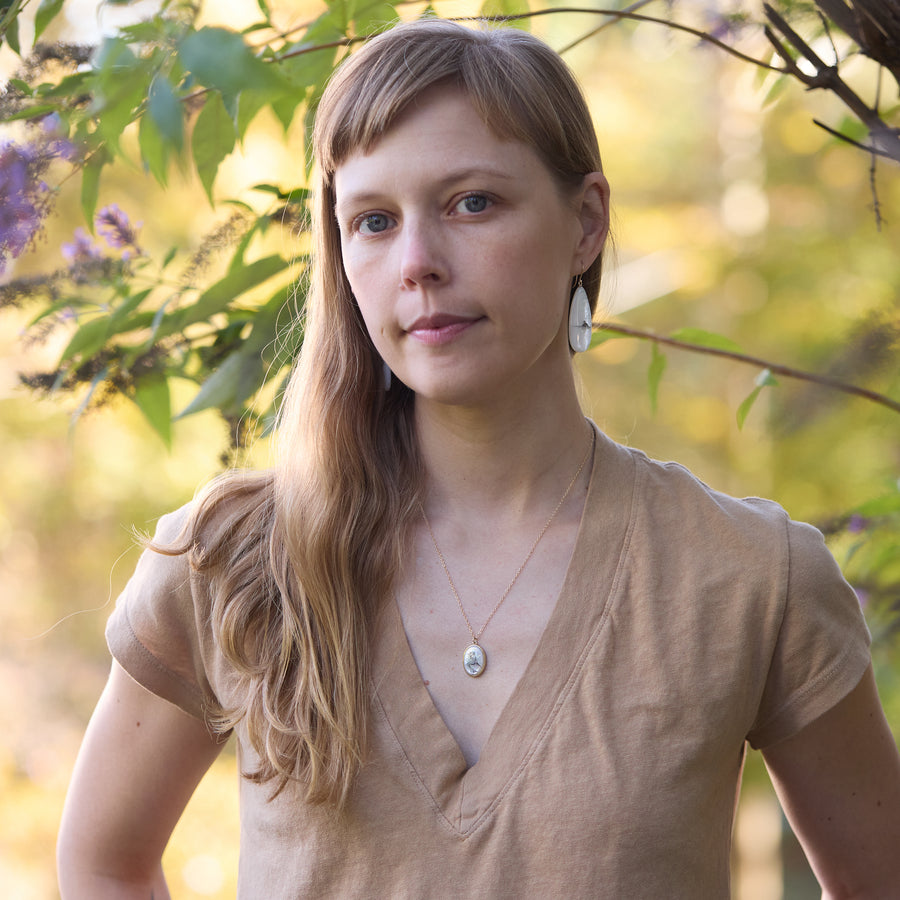 Woman standing outdoors with blurred greenery in the background