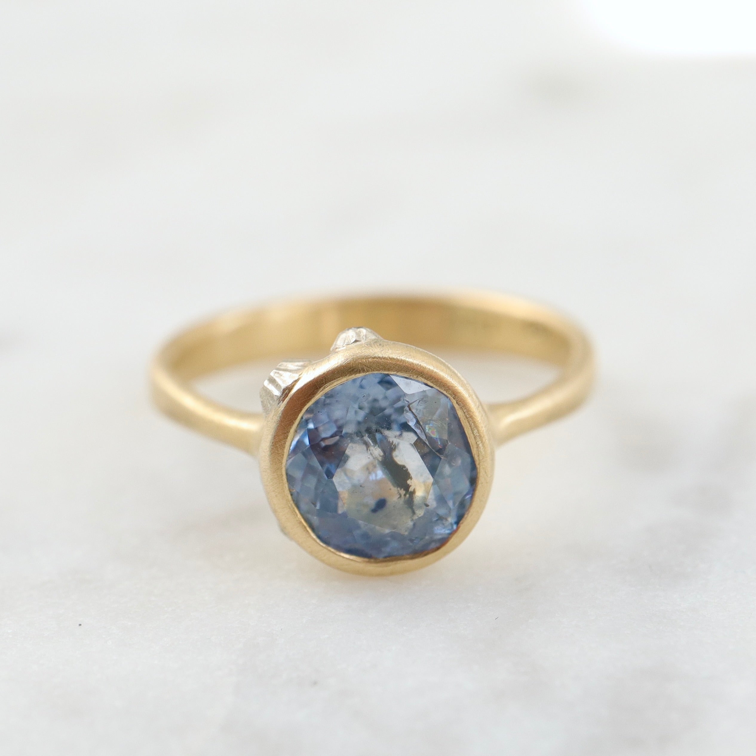 periwinkle sapphire set in a yellow gold ring with three white gold barnacles with diamonds. Front view.