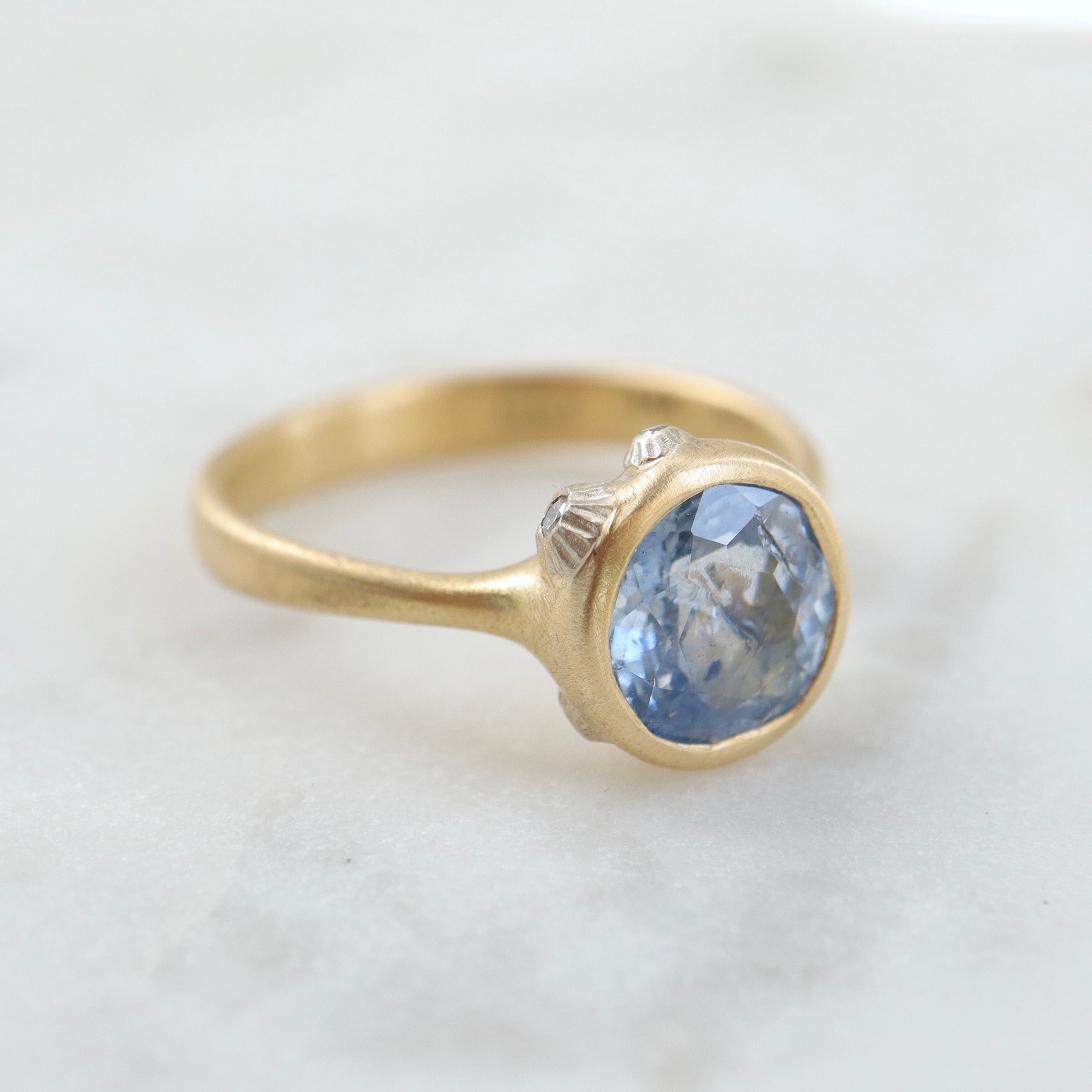 periwinkle sapphire set in a yellow gold ring with three white gold barnacles with diamonds. 1/4 view.