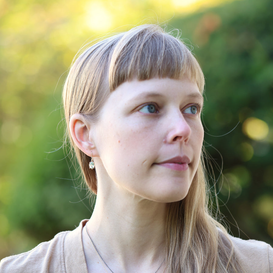 Woman with bangs wearing pale green earrings, looking to the side with a blurred green background