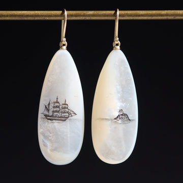 Teardrop-shaped mismatched earrings, a ship design on one and a mermaid on the other. on a black background