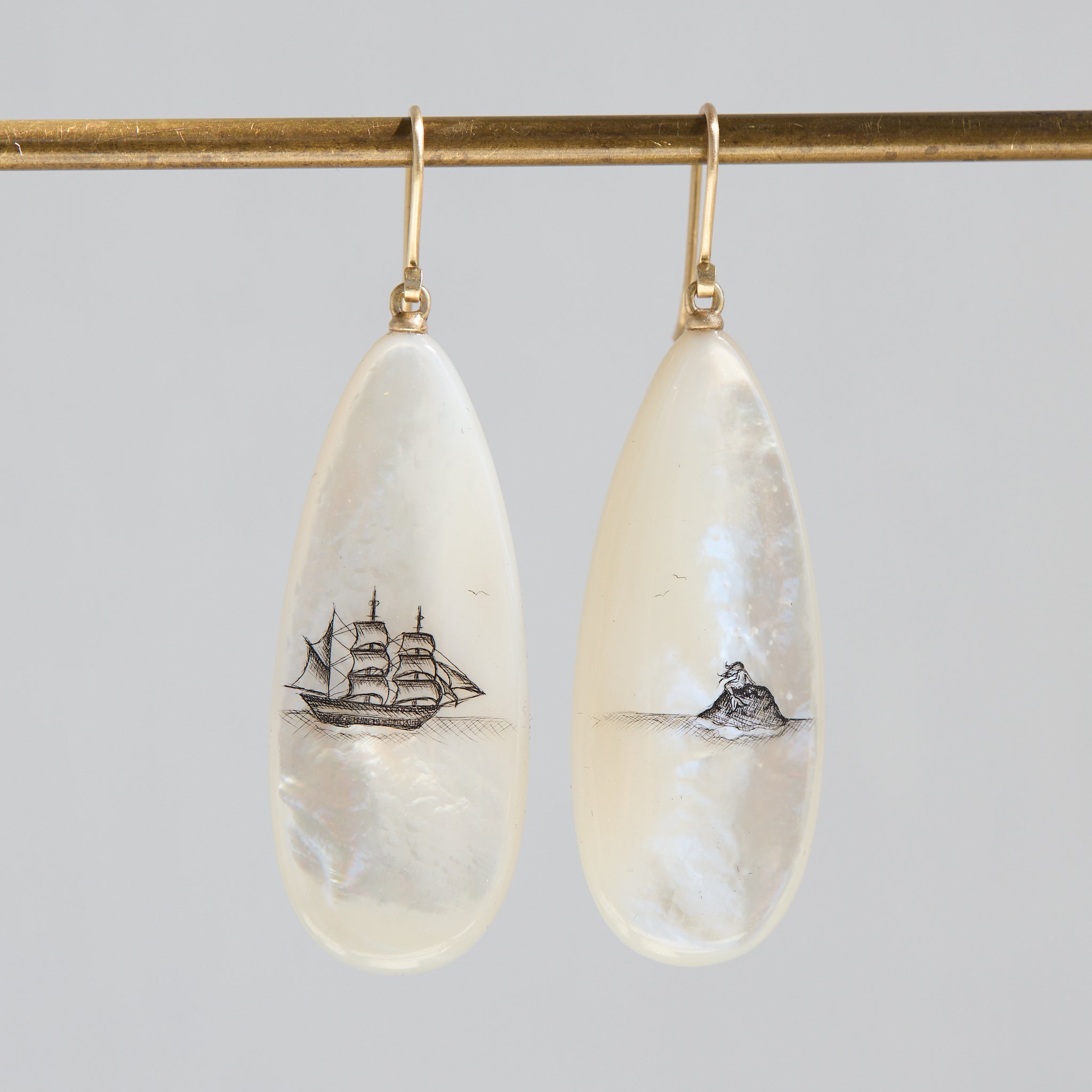 Teardrop-shaped mismatched earrings, a ship design on one and a mermaid on the other. 