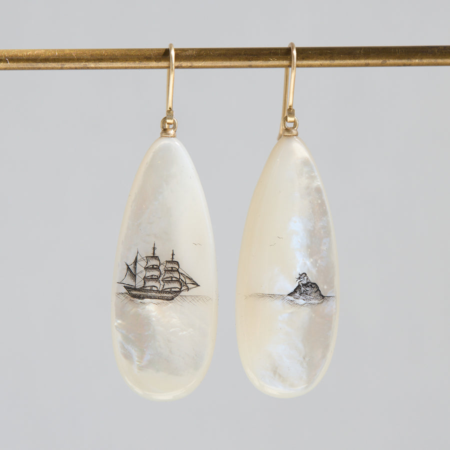 Teardrop-shaped mismatched earrings, a ship design on one and a mermaid on the other. 