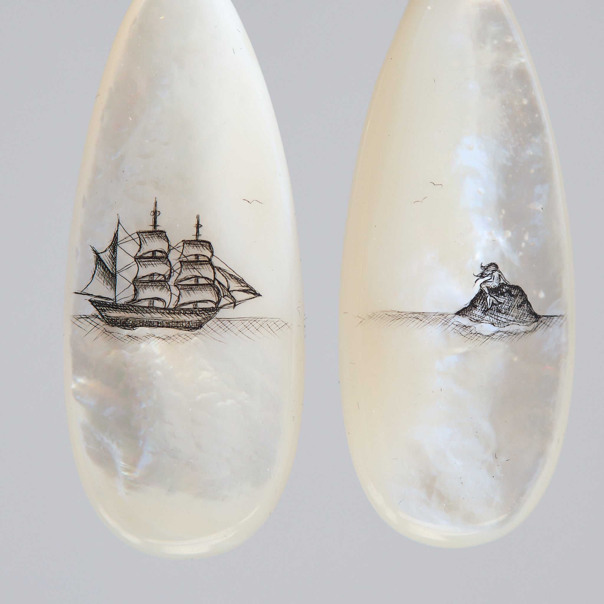 Teardrop-shaped mismatched earrings, a ship design on one and a mermaid on the other. 