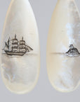 Teardrop-shaped mismatched earrings, a ship design on one and a mermaid on the other. 