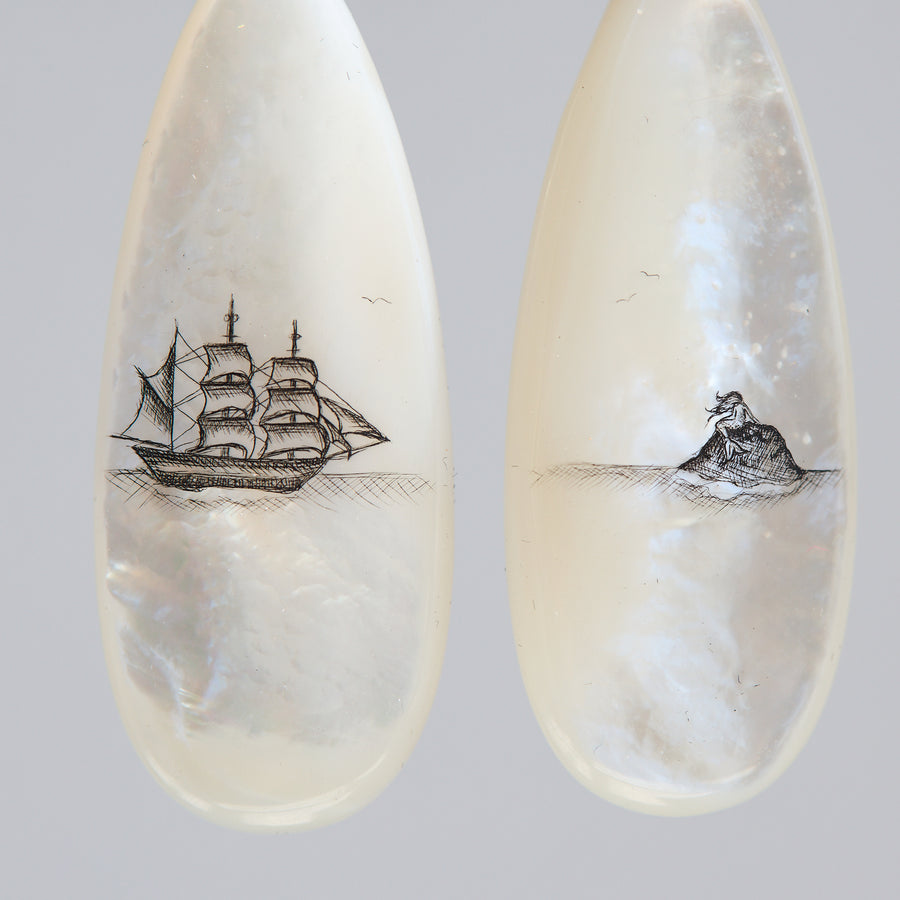 Teardrop-shaped mismatched earrings, a ship design on one and a mermaid on the other. 