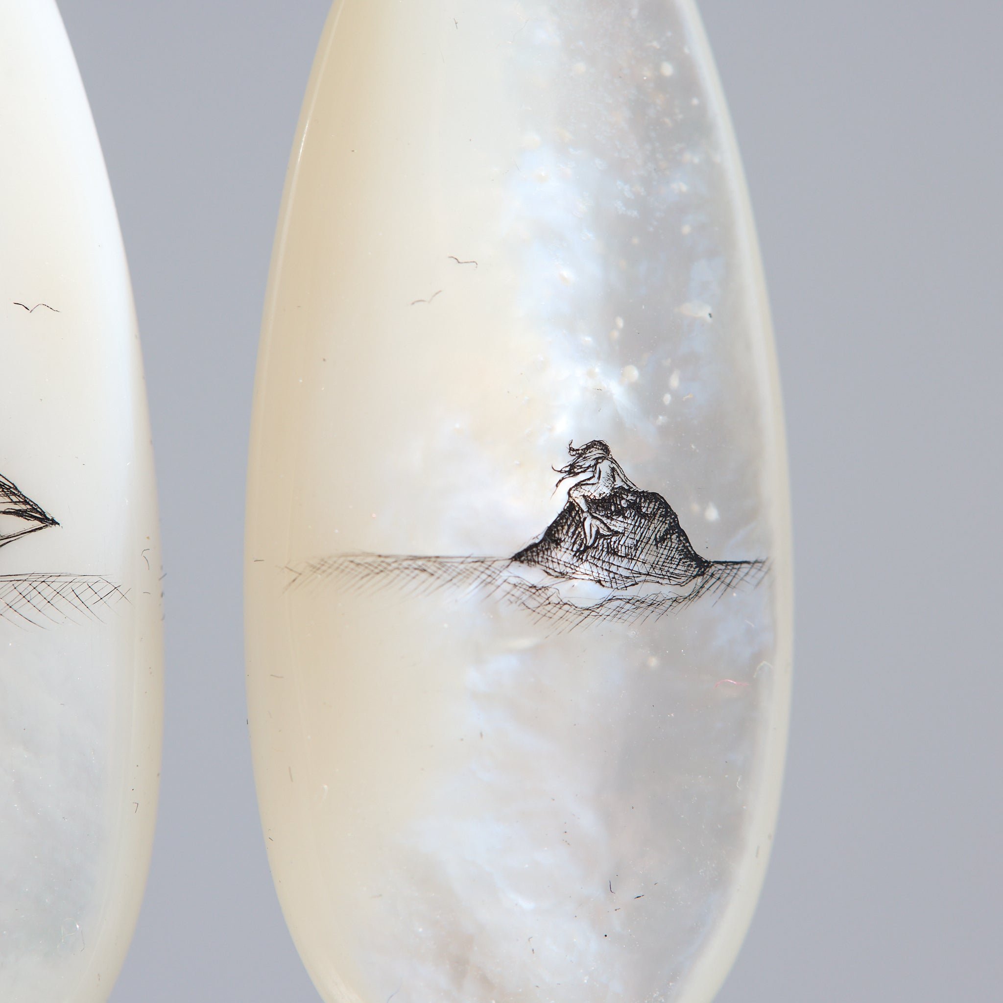 Teardrop-shaped mismatched earrings, a ship design on one and a mermaid on the other. 