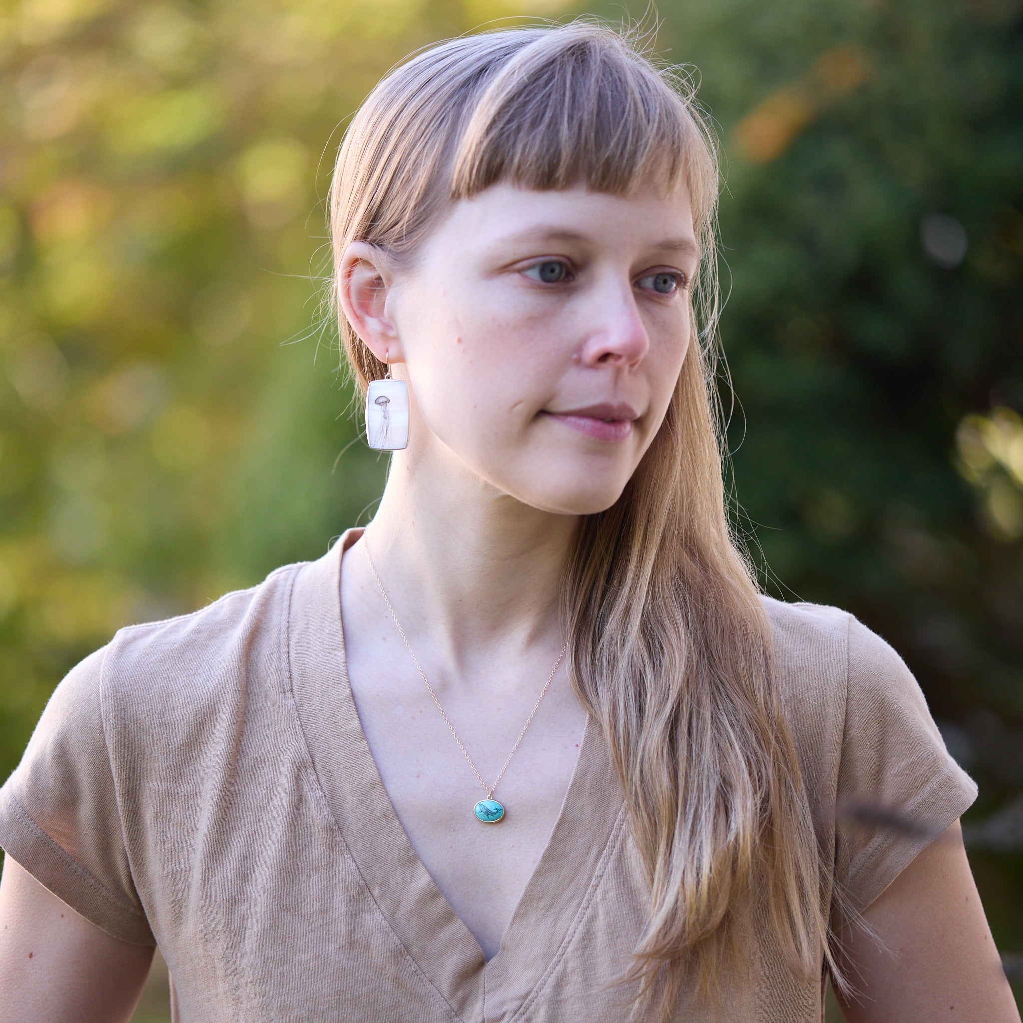 Woman wearing earrings and a necklace outdoors with a blurred green background