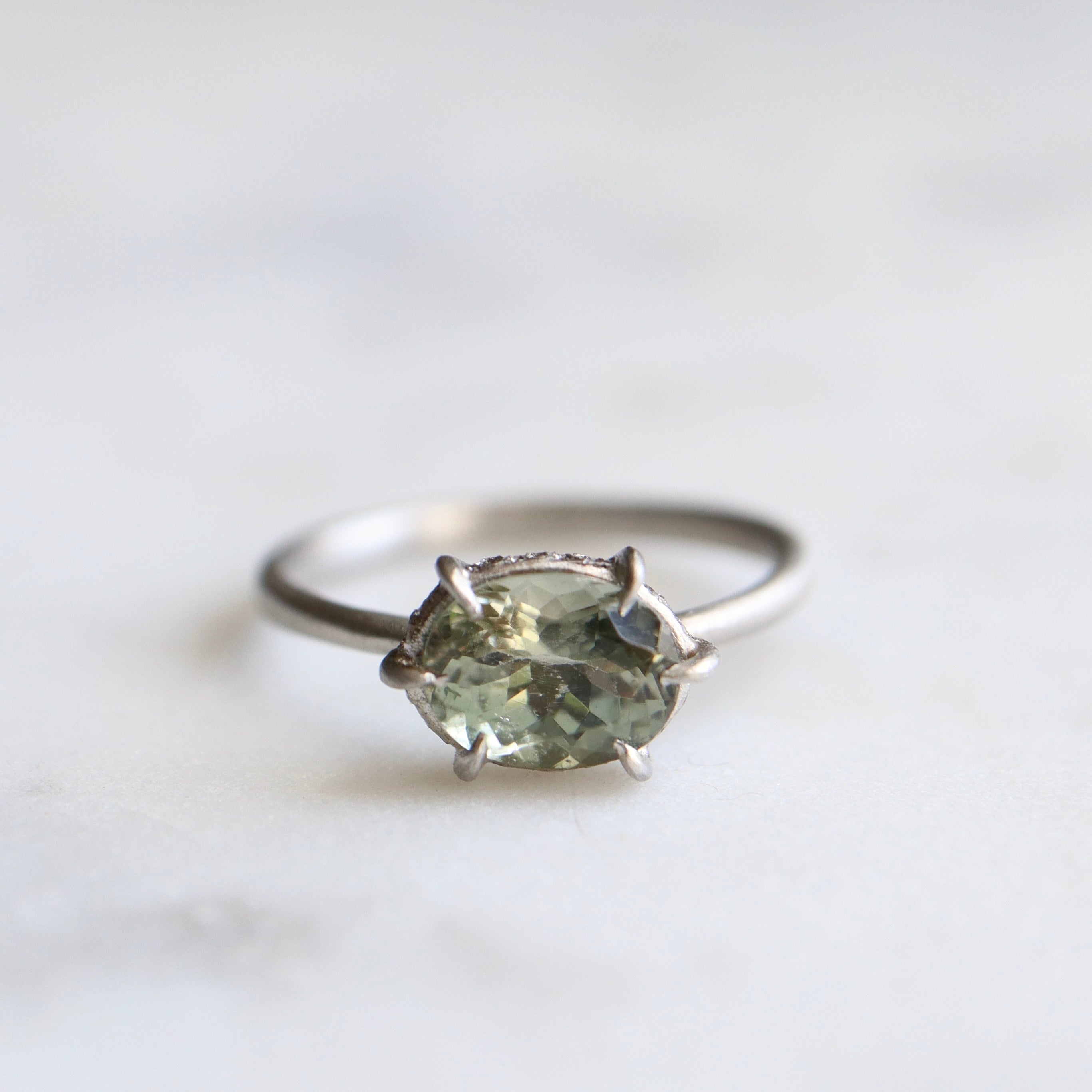 grey oval tourmaline stone set in a platinum ring with gold prongs and diamonds set around the seat.