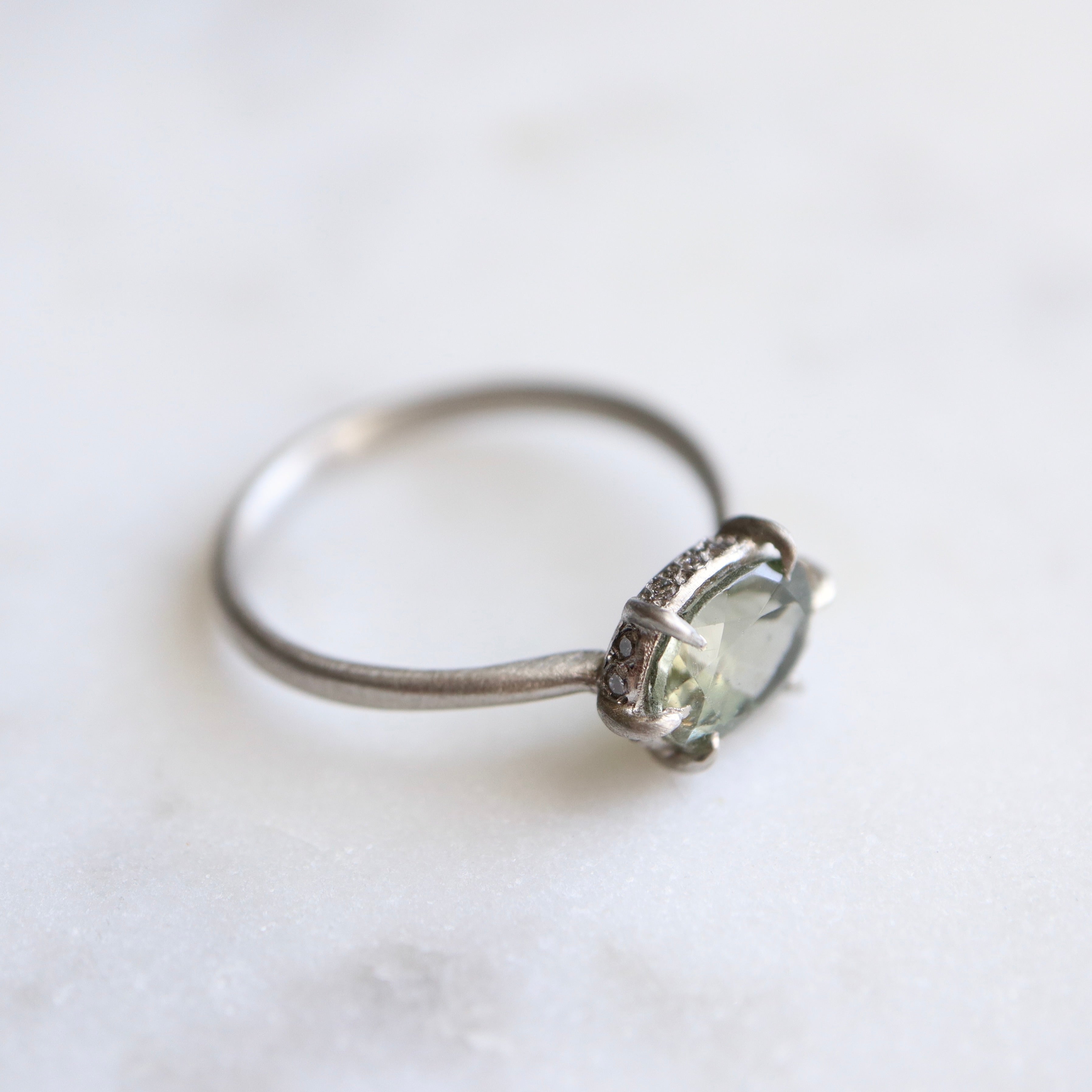 grey oval tourmaline stone set in a platinum ring with gold prongs and diamonds set around the seat. side view.