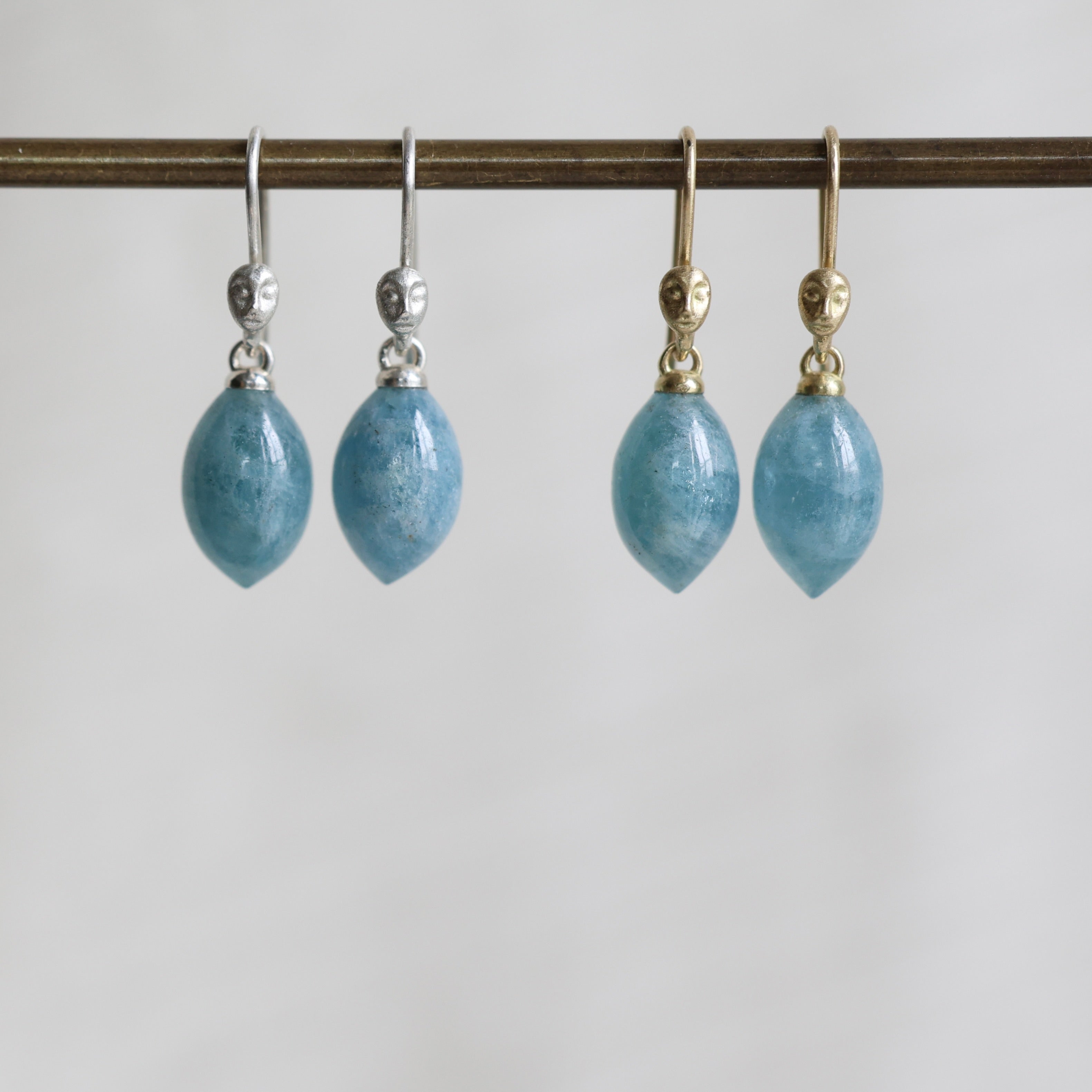 two pairs of blue teardrop earrings on a metal rod against a white background