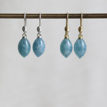 two pairs of blue teardrop earrings on a metal rod against a white background